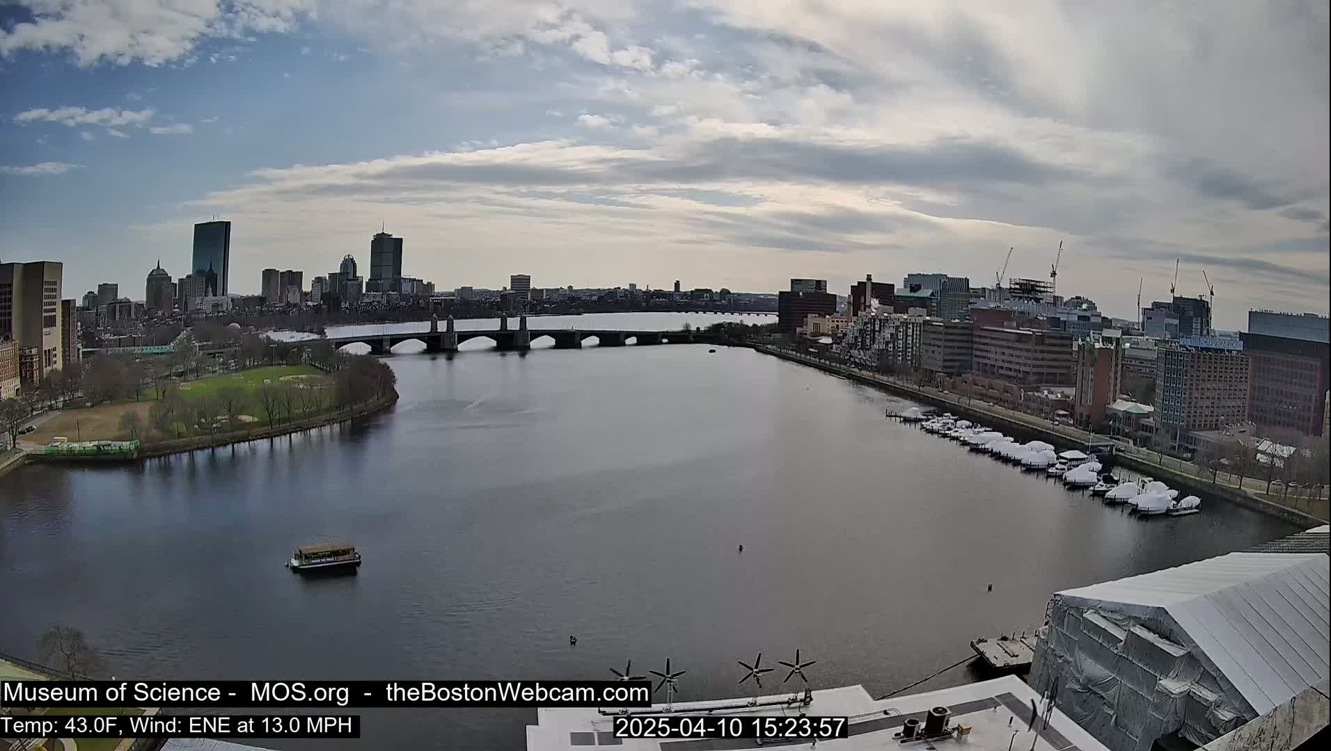 A city skyline with a bridge over a river, under a partly cloudy sky.