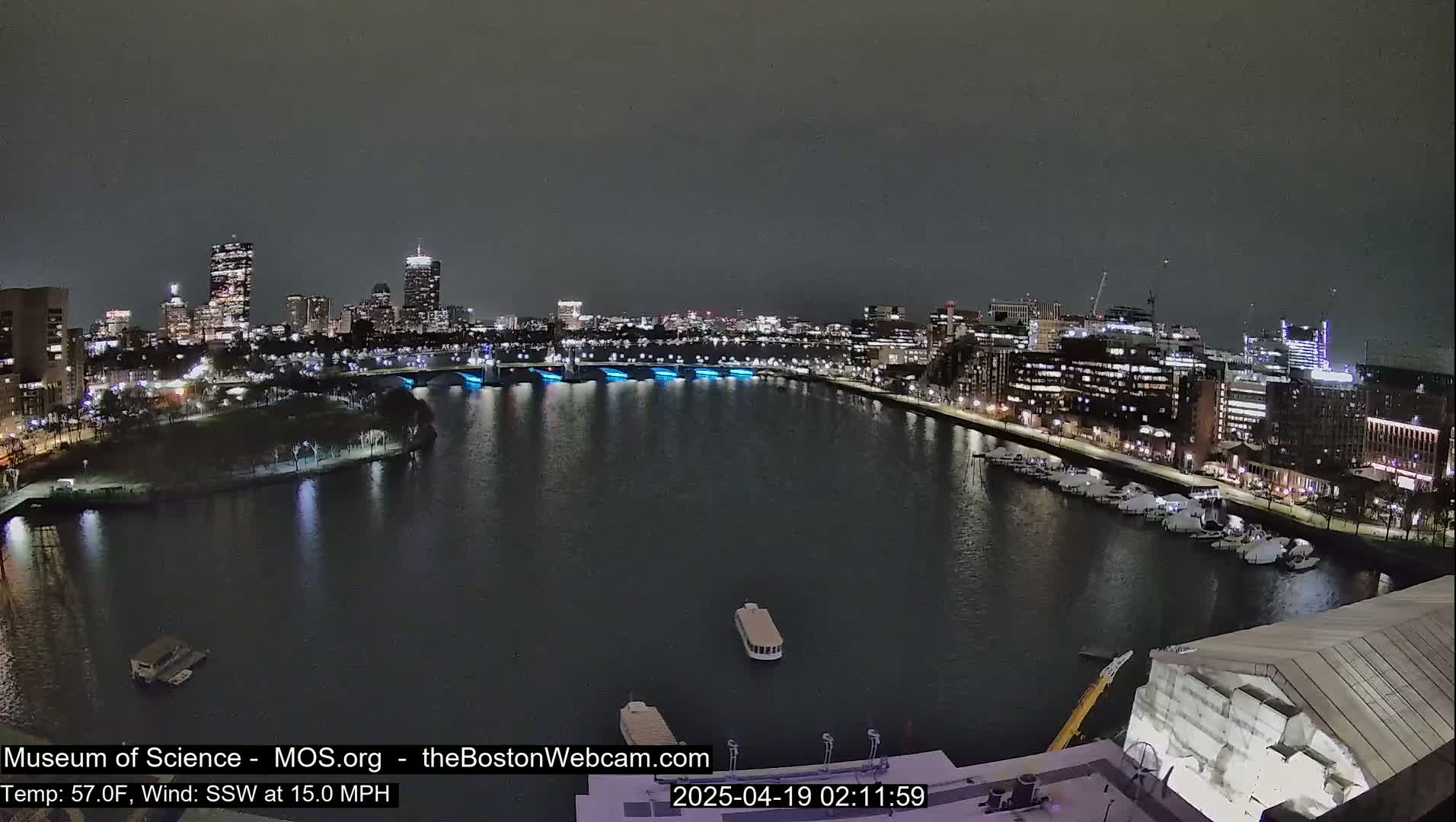 A nighttime cityscape with a river, lit bridges, and docked boats under a dark sky.