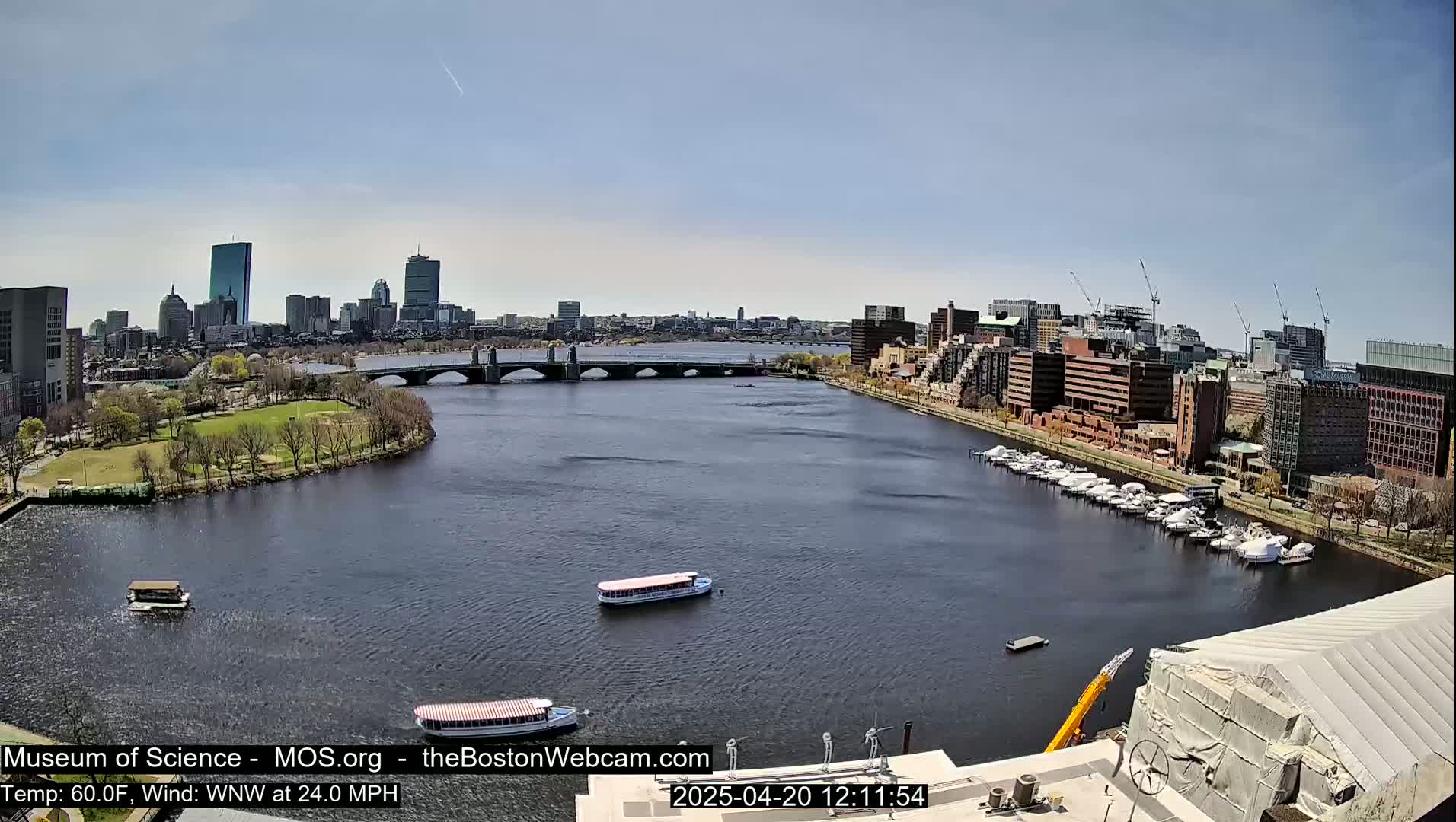 A city skyline with several bridges and boats on a river, under a clear sunny sky with a brisk wind.