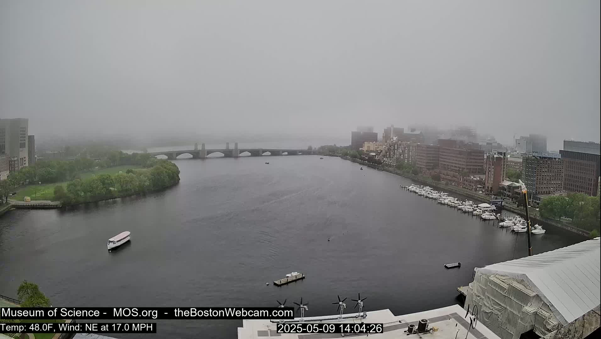 A foggy view of a river with a bridge, boats, and buildings on either side.