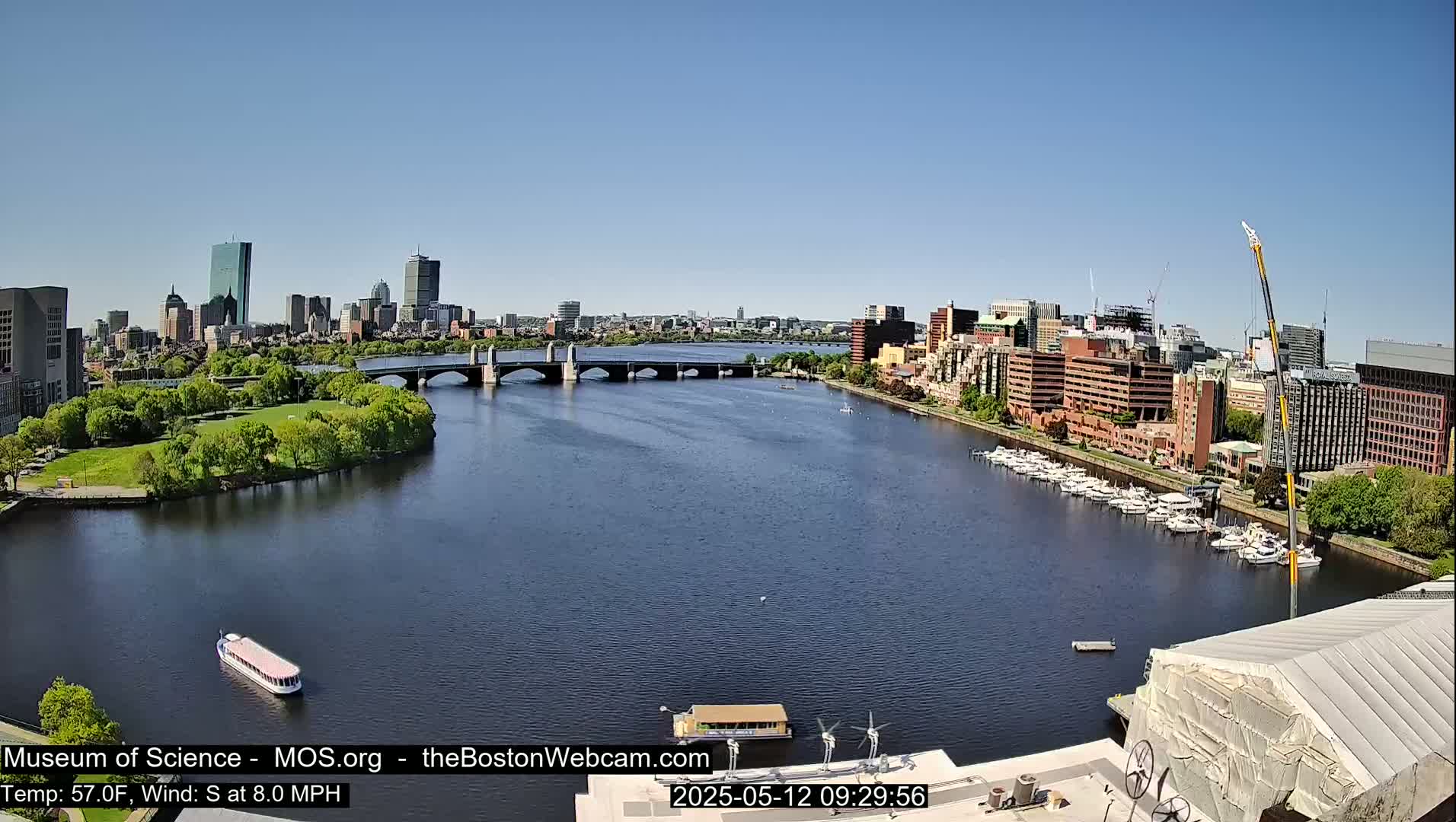 A river flows under a bridge toward a city skyline on a sunny day with a south wind.