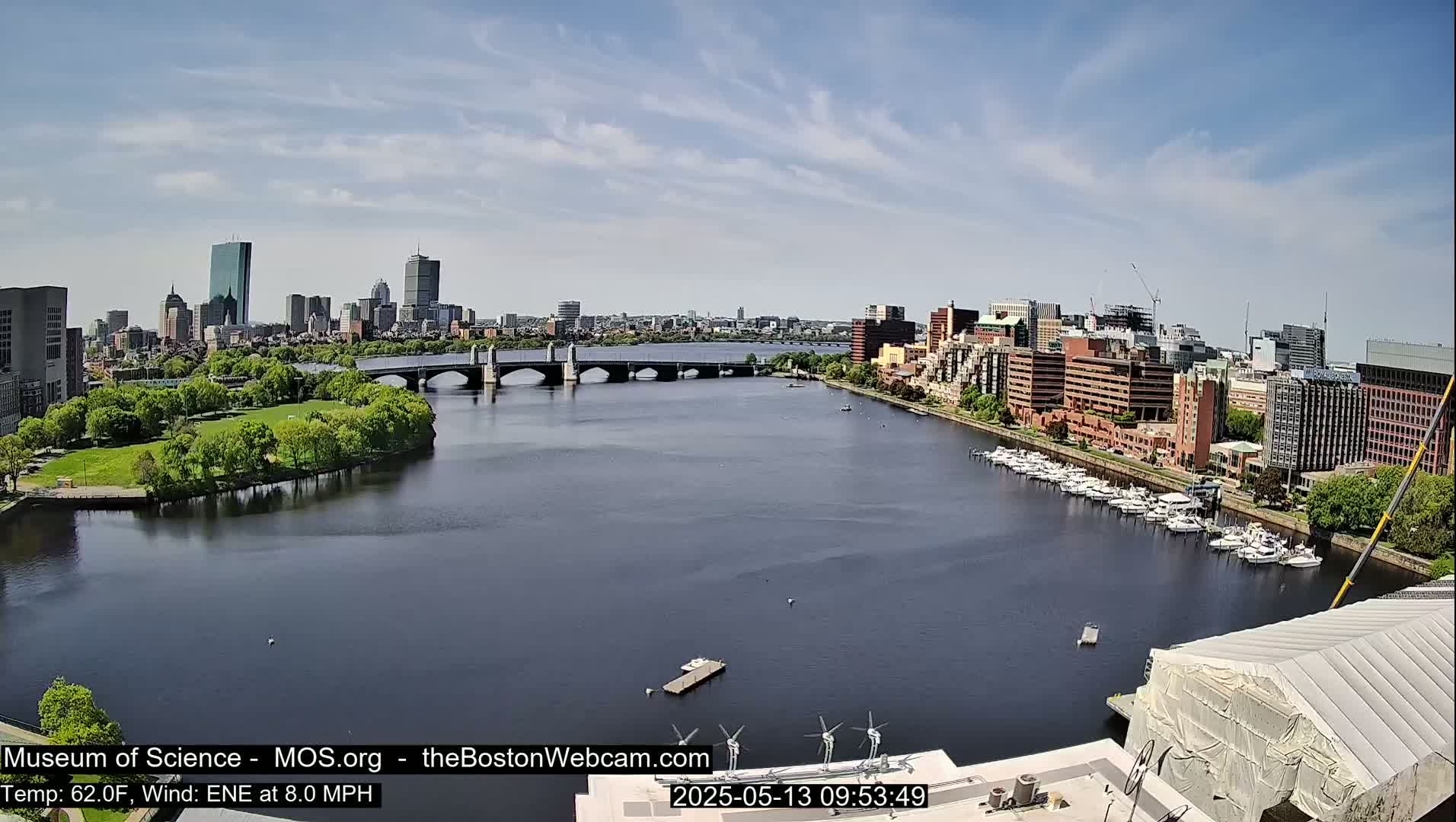 A city skyline with several buildings, a bridge spanning a river, and a marina with numerous boats is visible under a mostly clear sky.