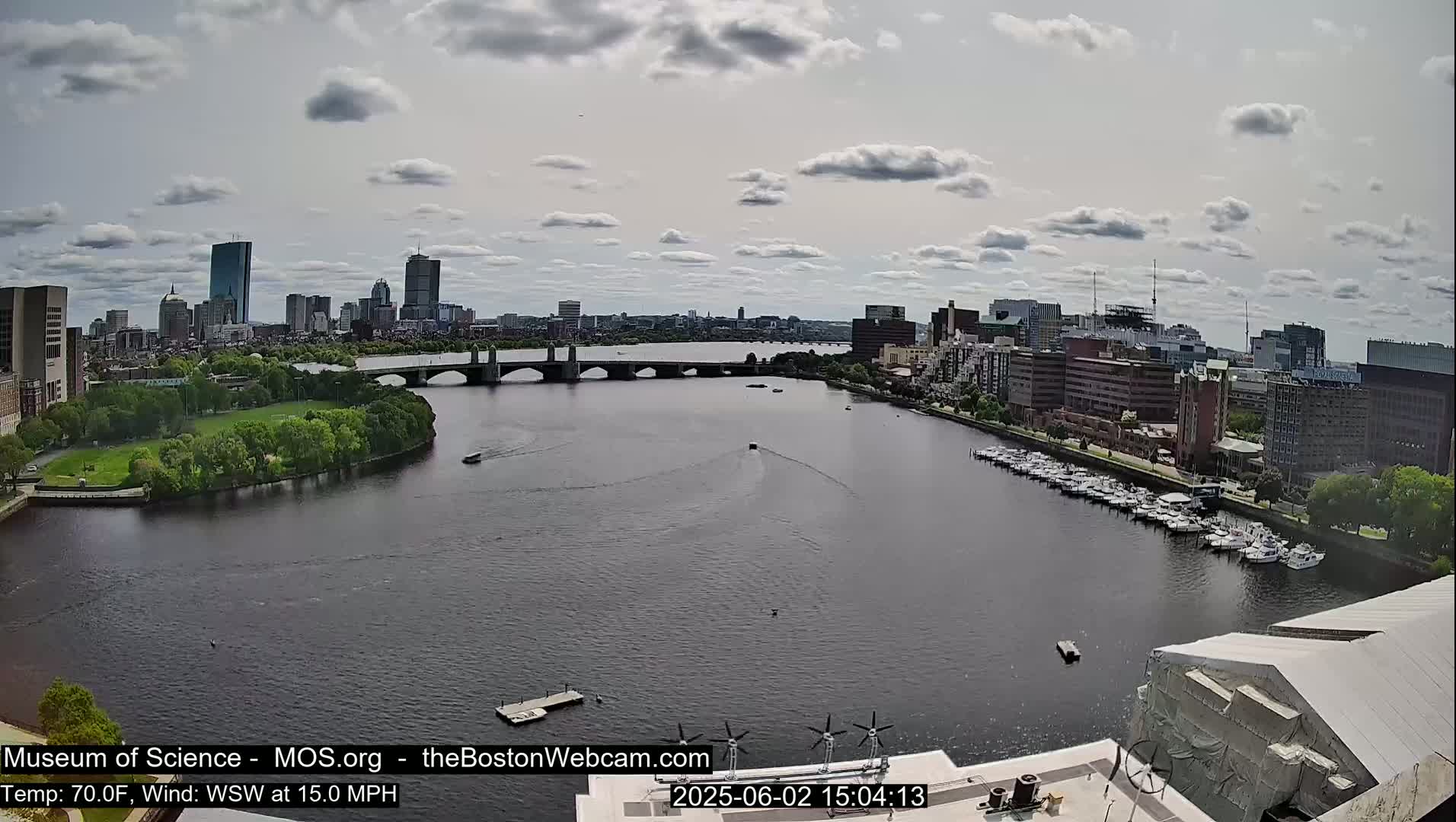 A cityscape with a river, bridge, and boats under a partly cloudy sky.