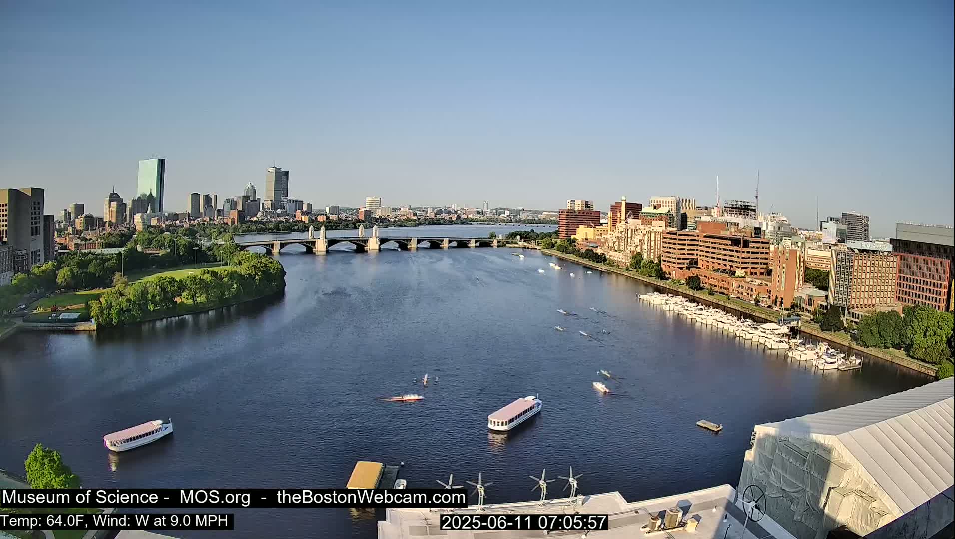 A sunny day reveals a cityscape across a river, with several boats and bridges in view, under a clear sky.