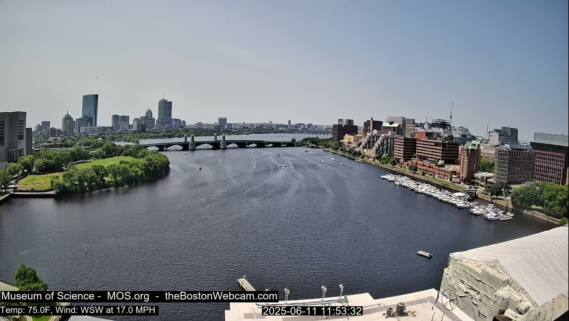 A sunny cityscape with a river, bridge, and numerous boats is visible under a clear sky.
