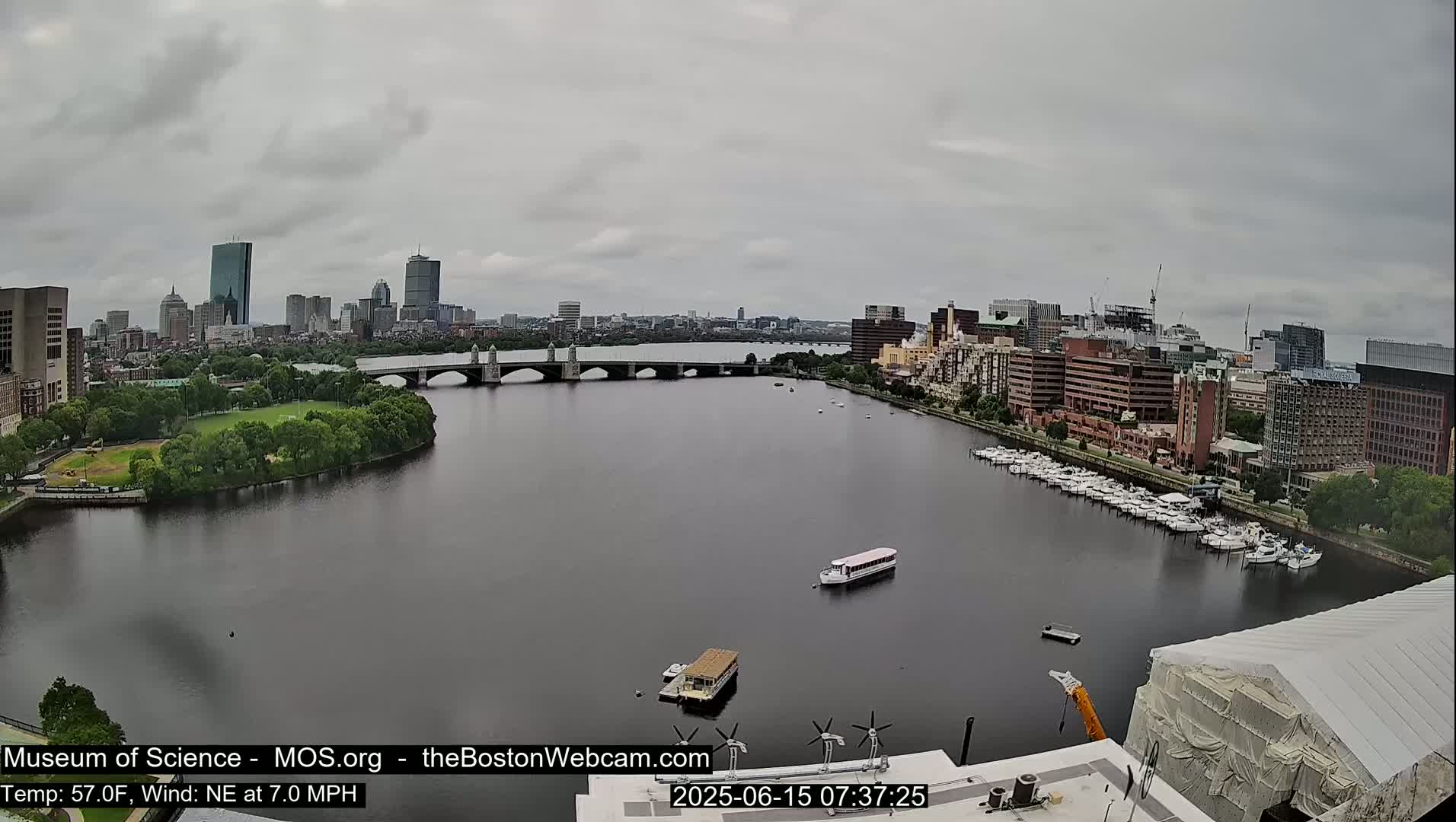 A wide shot of a river with a bridge and city skyline under an overcast sky.