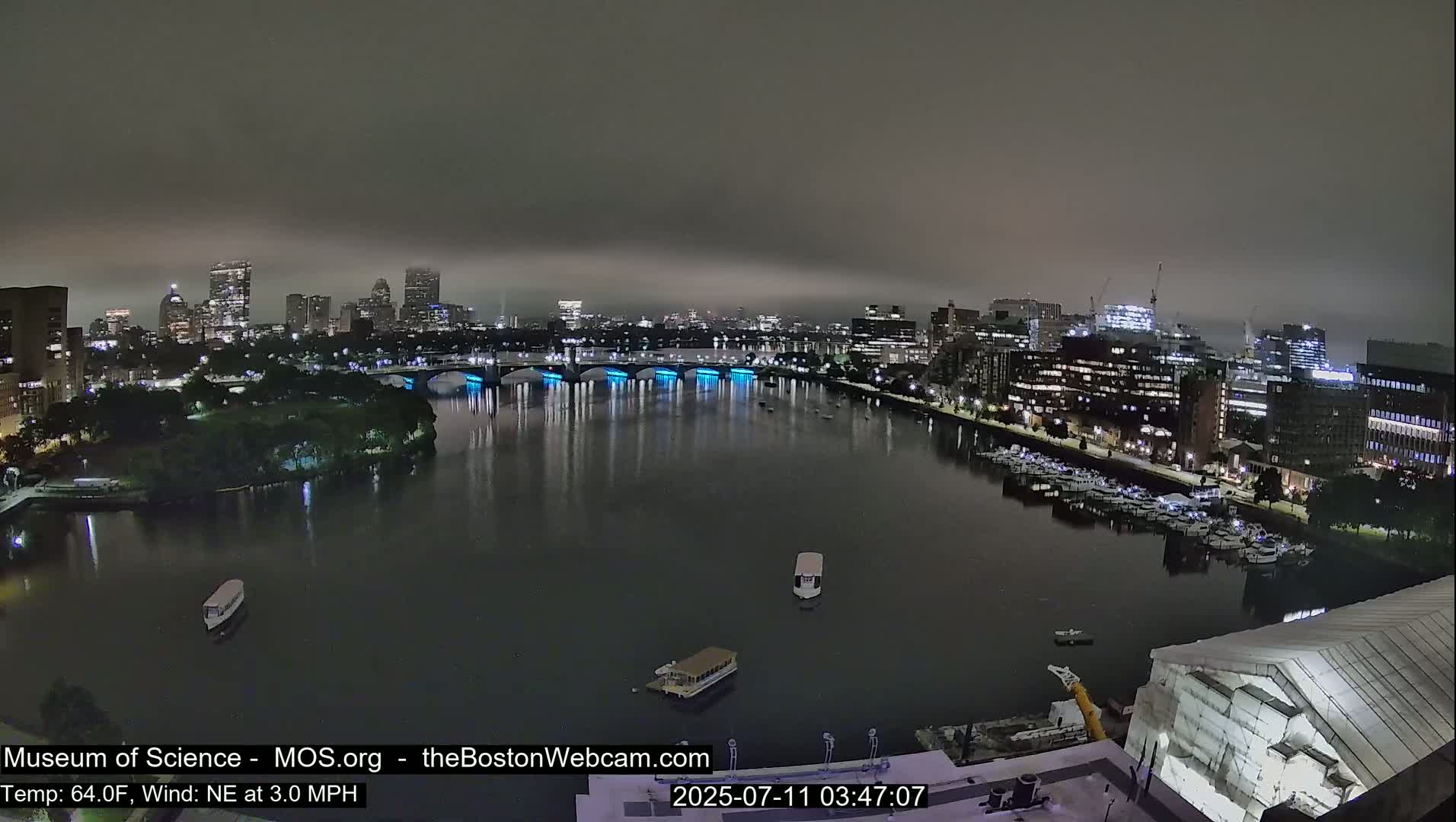 A nighttime view of a city skyline across a river, under a foggy sky.