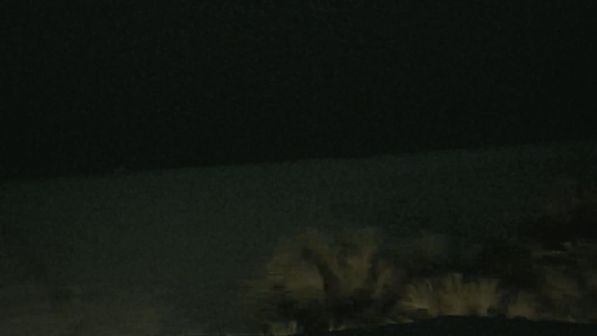 A dark, nighttime scene shows a body of water under a mostly clear, dark sky with some vegetation visible in the bottom right corner.