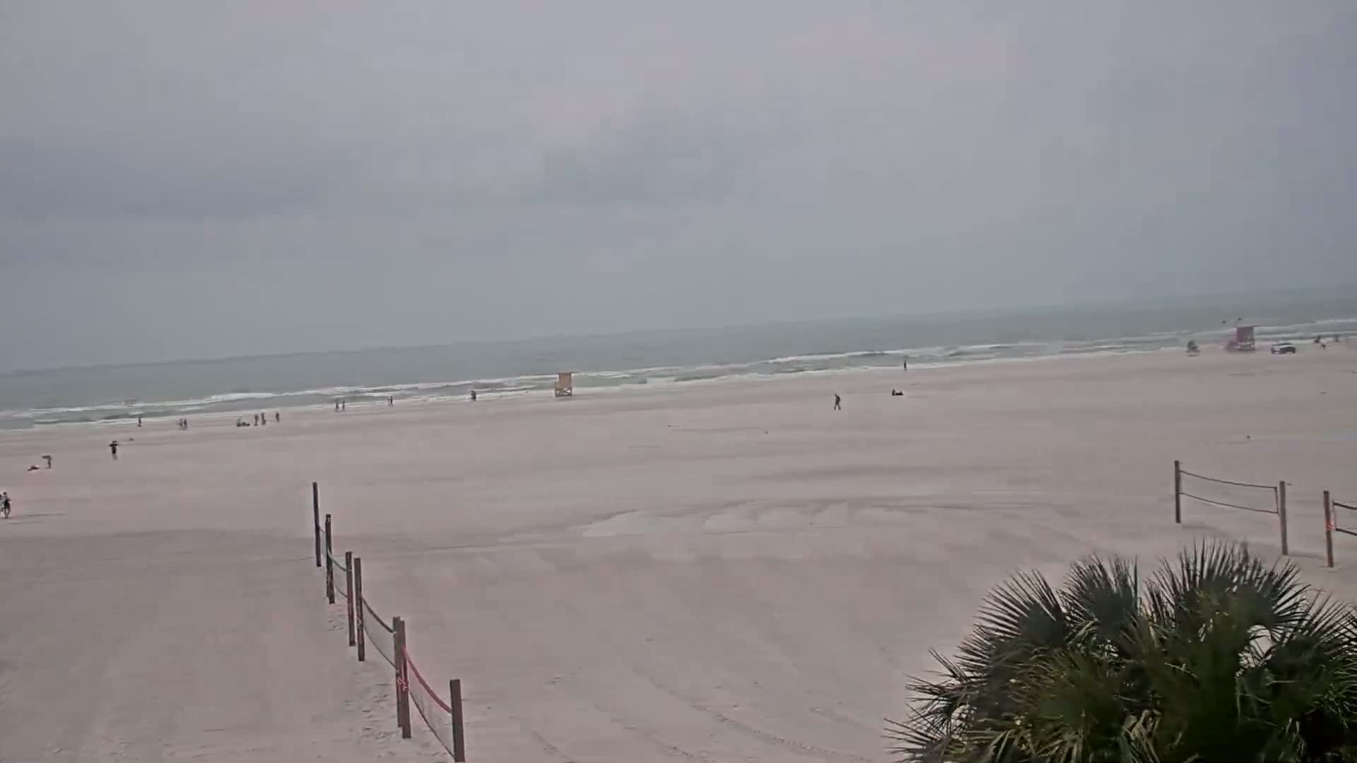 A mostly empty, sandy beach stretches to a grey, overcast ocean under a cloudy sky.