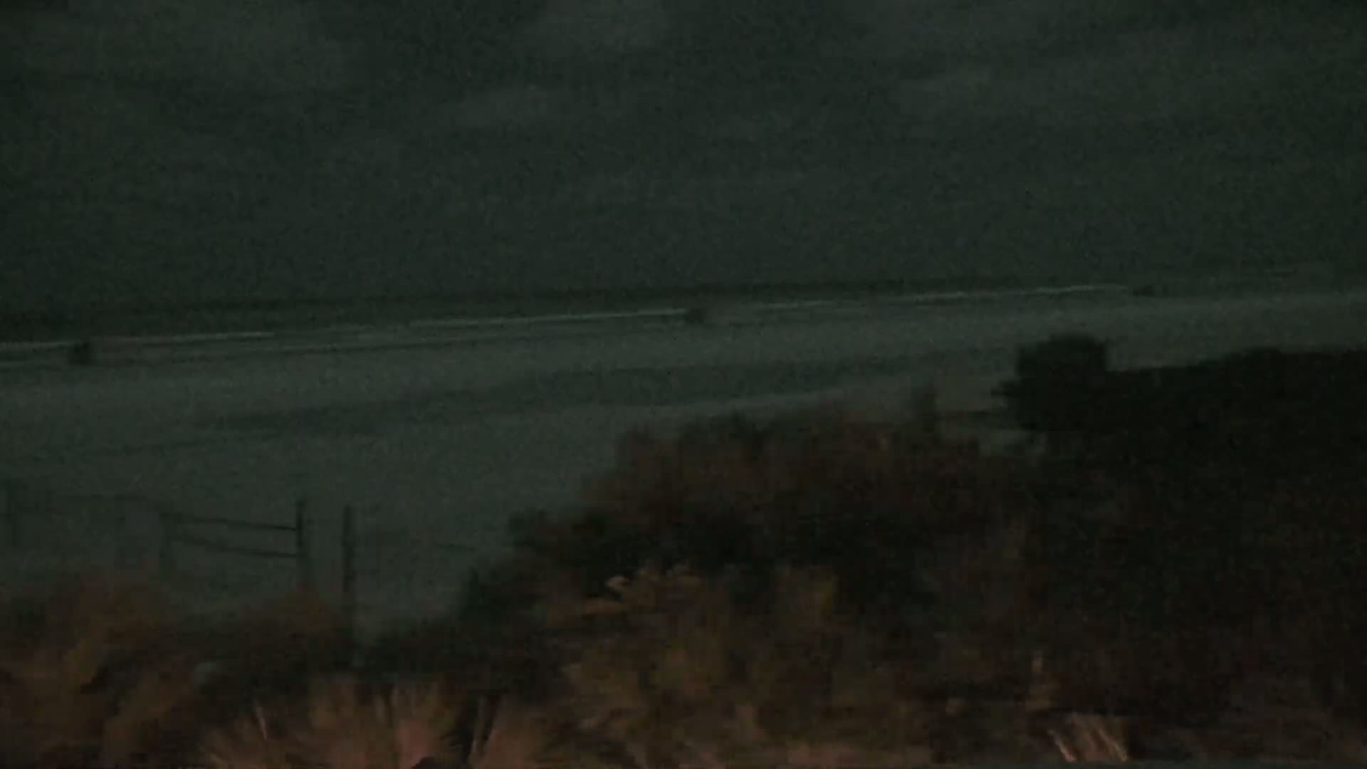 A dark, nighttime view shows a beach and ocean under an overcast sky.