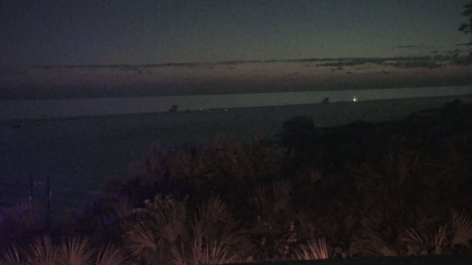 A dark, nighttime view shows a body of water under a dusky sky with a faint, pinkish-purple horizon.