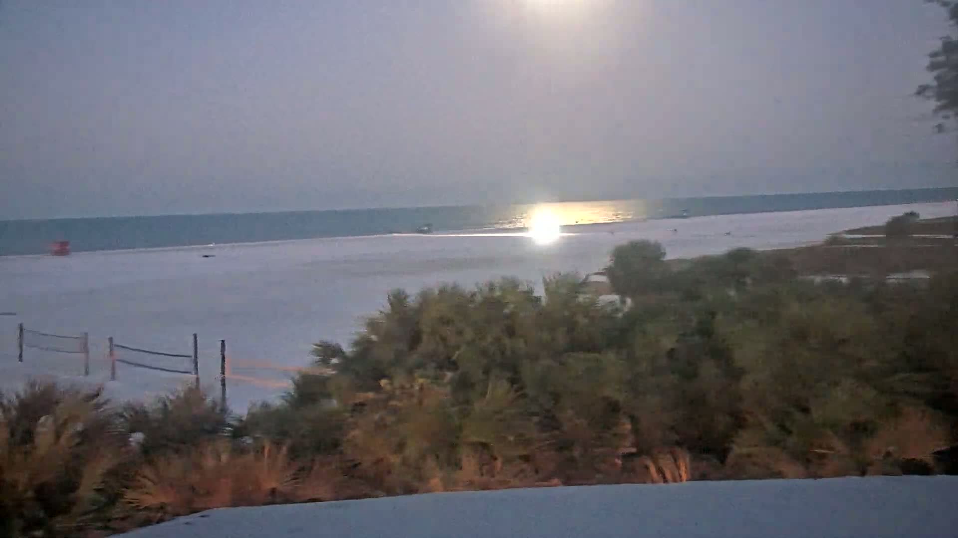 A moonlit beach scene shows a calm ocean, a wide expanse of sand with a volleyball net, and vegetation in the foreground.