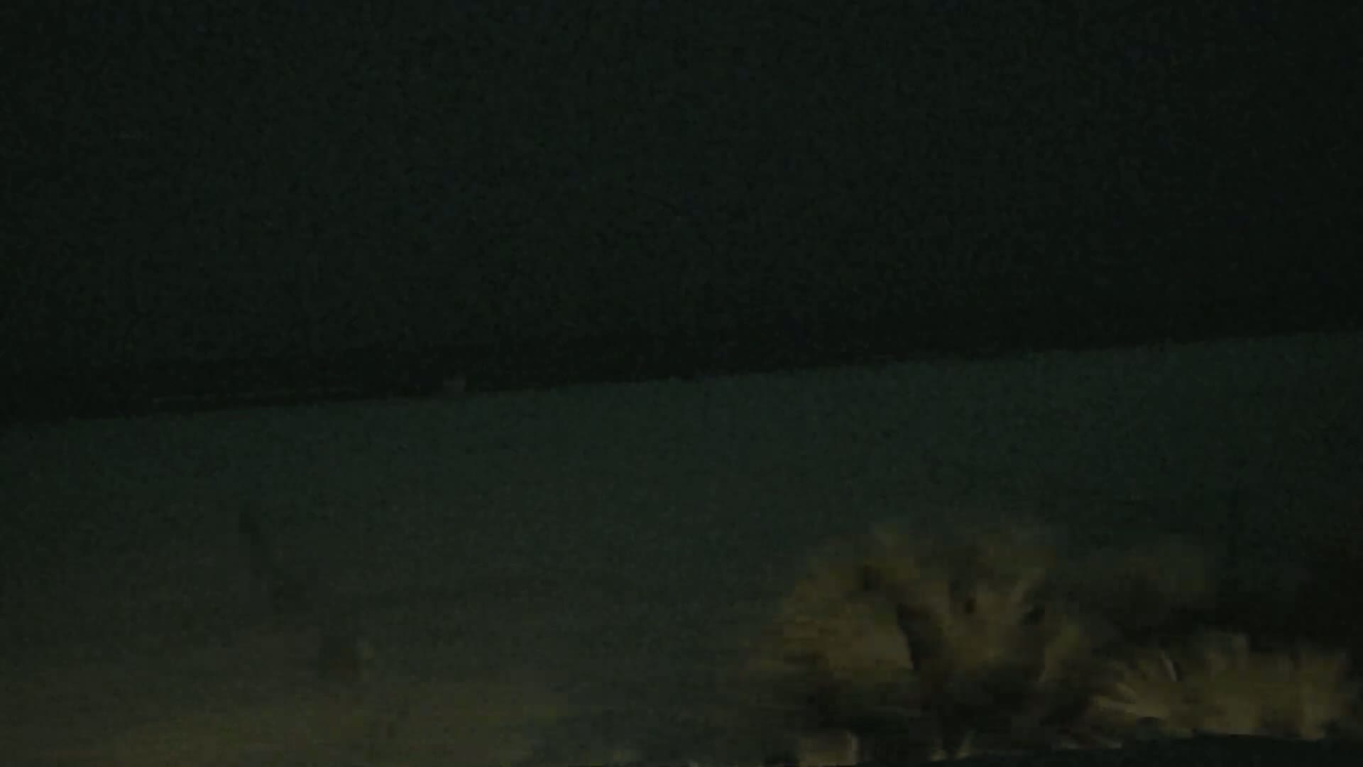 A low-light nighttime image shows a tan-colored plume of dust or smoke rising from a dark surface.