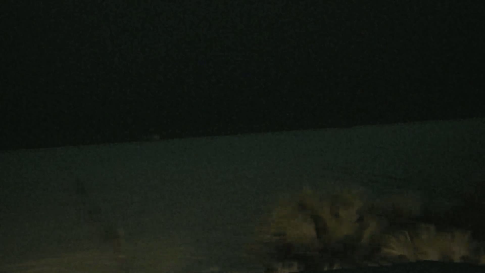 At night, waves crash on a dark shoreline under a dark sky.