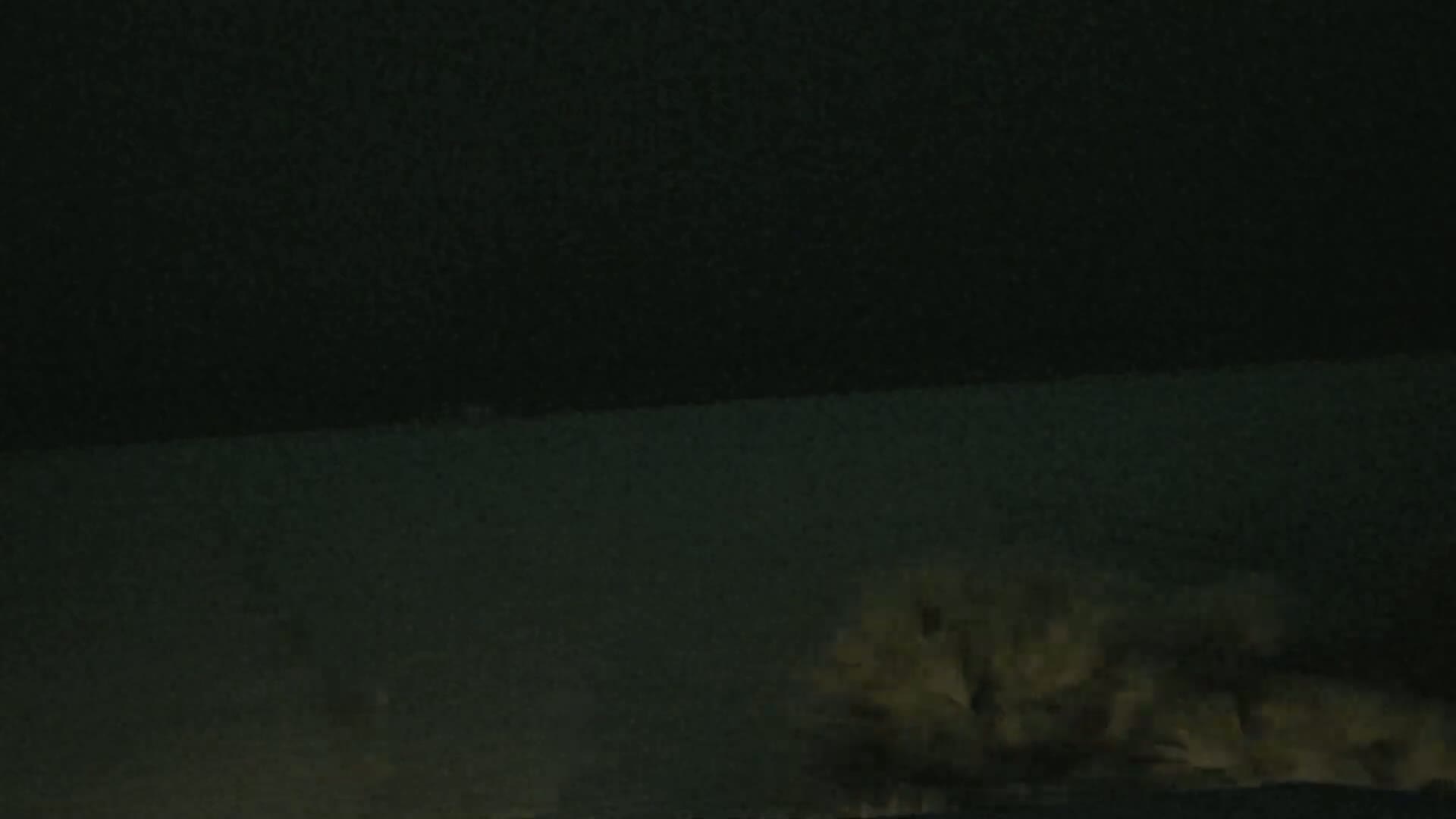 A dark, nighttime scene shows a body of water and indistinct, light-colored vegetation in the lower right corner.