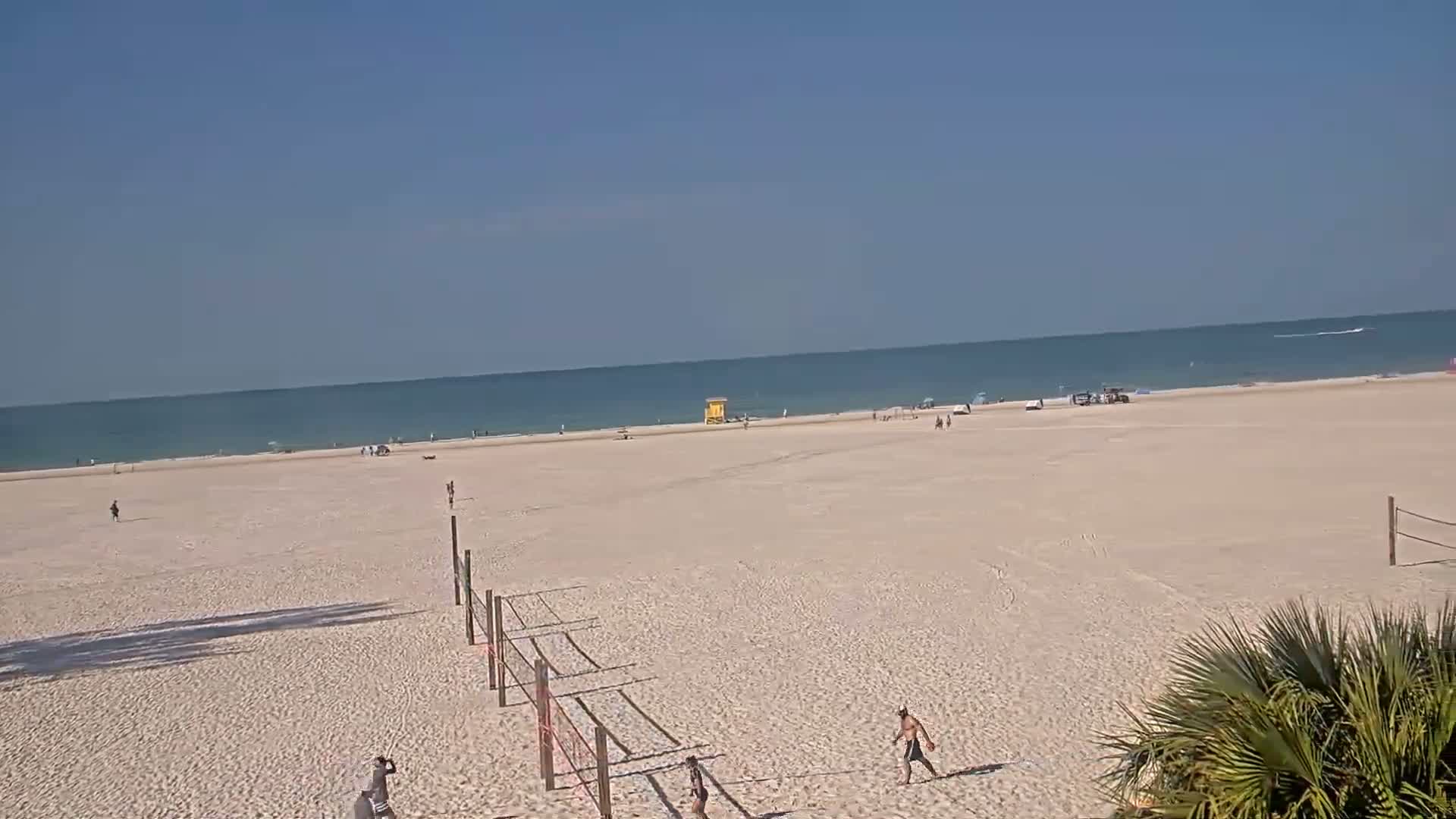 A mostly empty sandy beach stretches to a calm ocean under a clear blue sky.