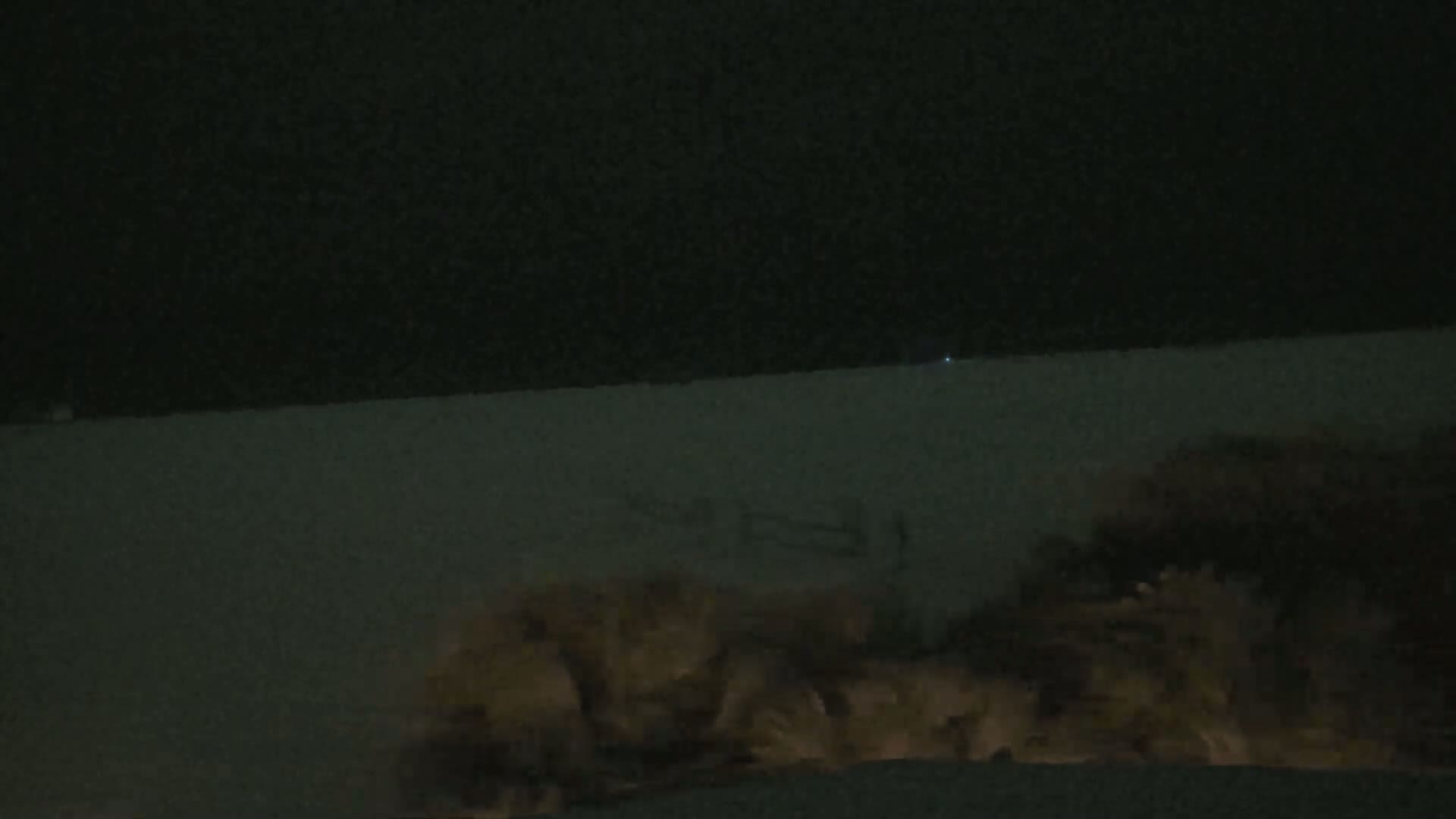 At night, a low-light image shows dark water or a dark surface with lighter, possibly foamy, material at the bottom.
