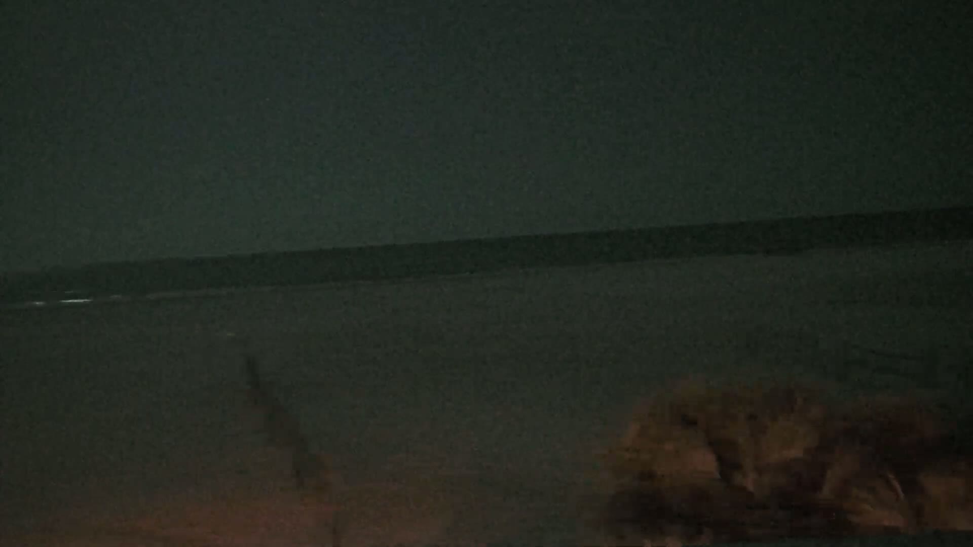 A dark, nighttime beach scene shows a calm ocean and some vegetation in the lower right corner.