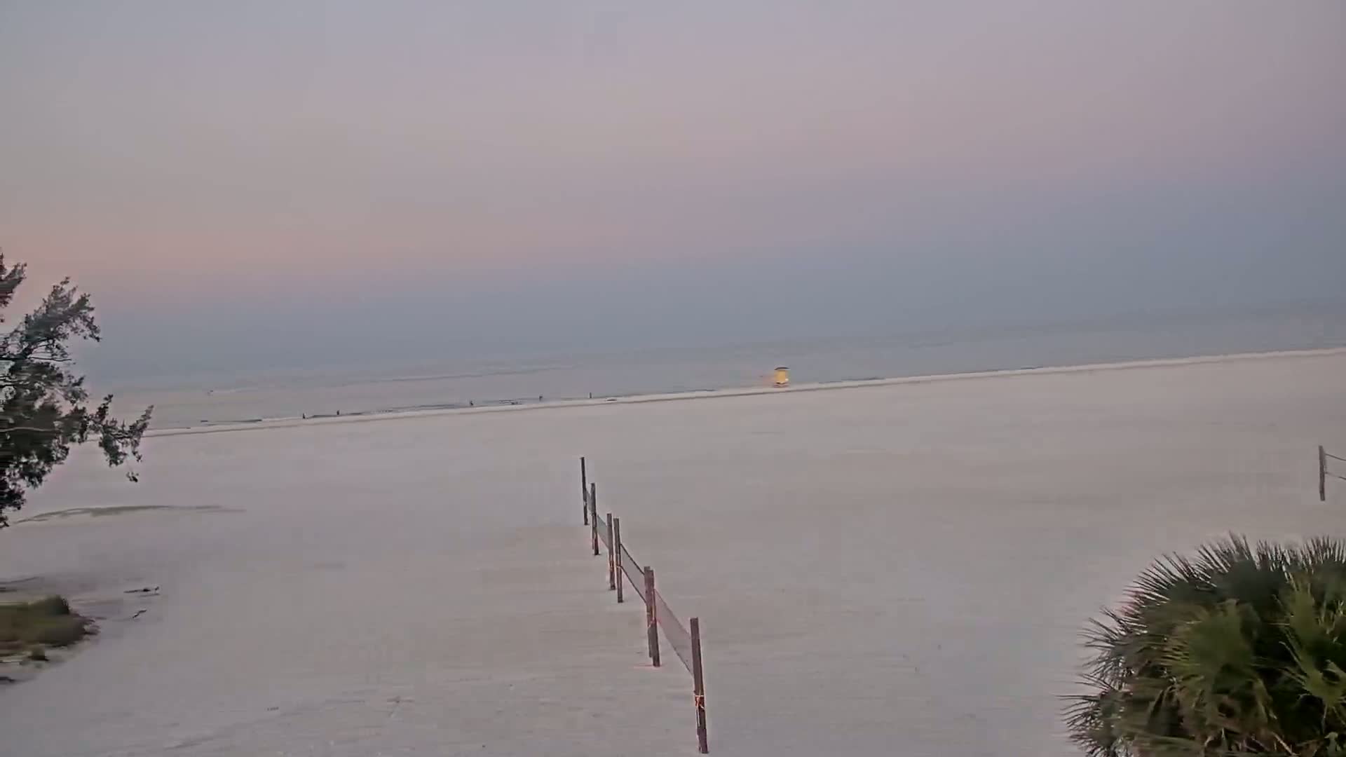 A mostly empty, light-colored sandy beach stretches to a calm, hazy ocean under a pale, overcast sky.