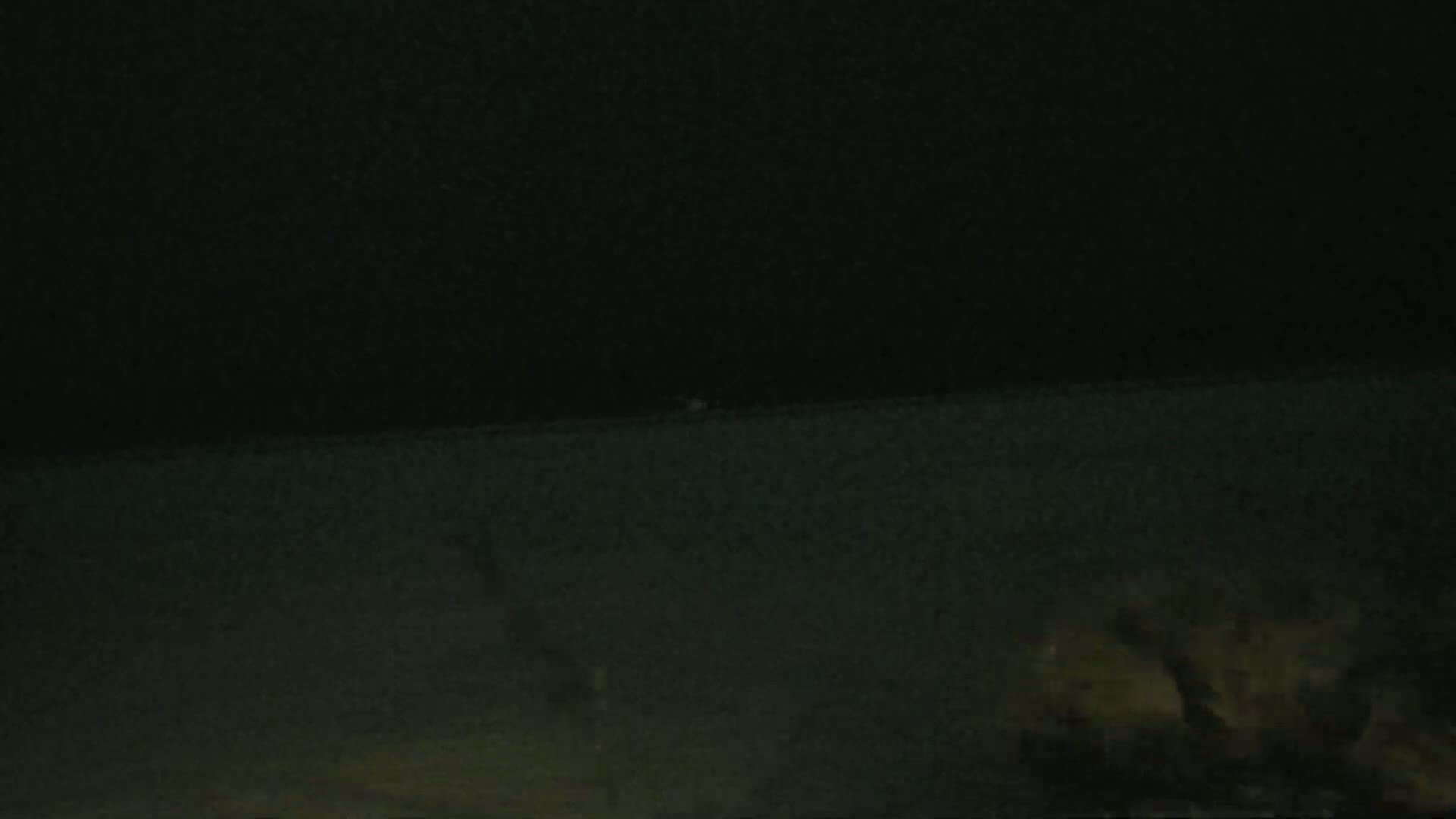 A dark, nighttime scene shows a flat, dark surface, possibly ground or water, with indistinct shapes in the lower right corner.