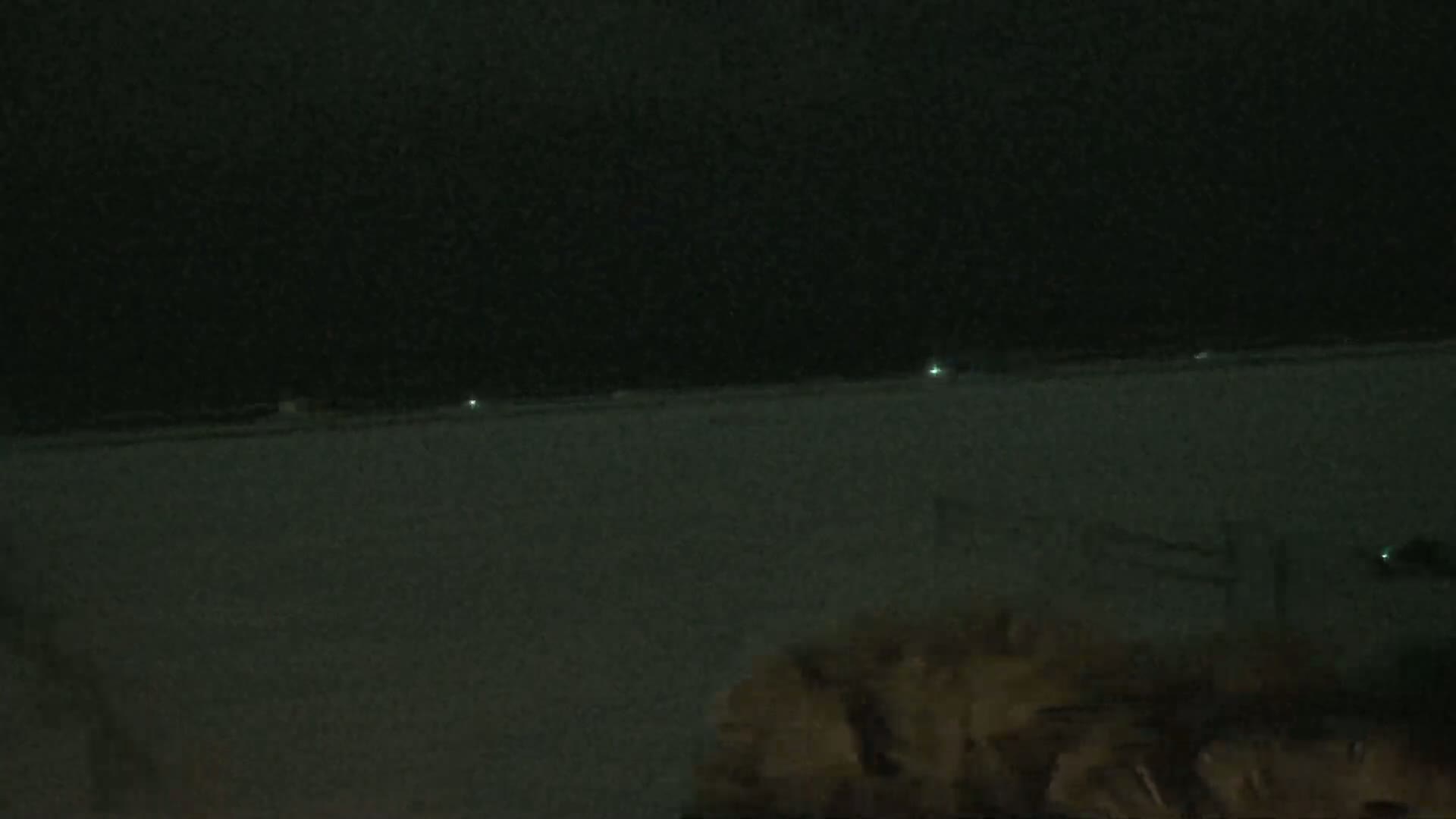 A snow-covered landscape is visible at night, with faint lights in the distance.