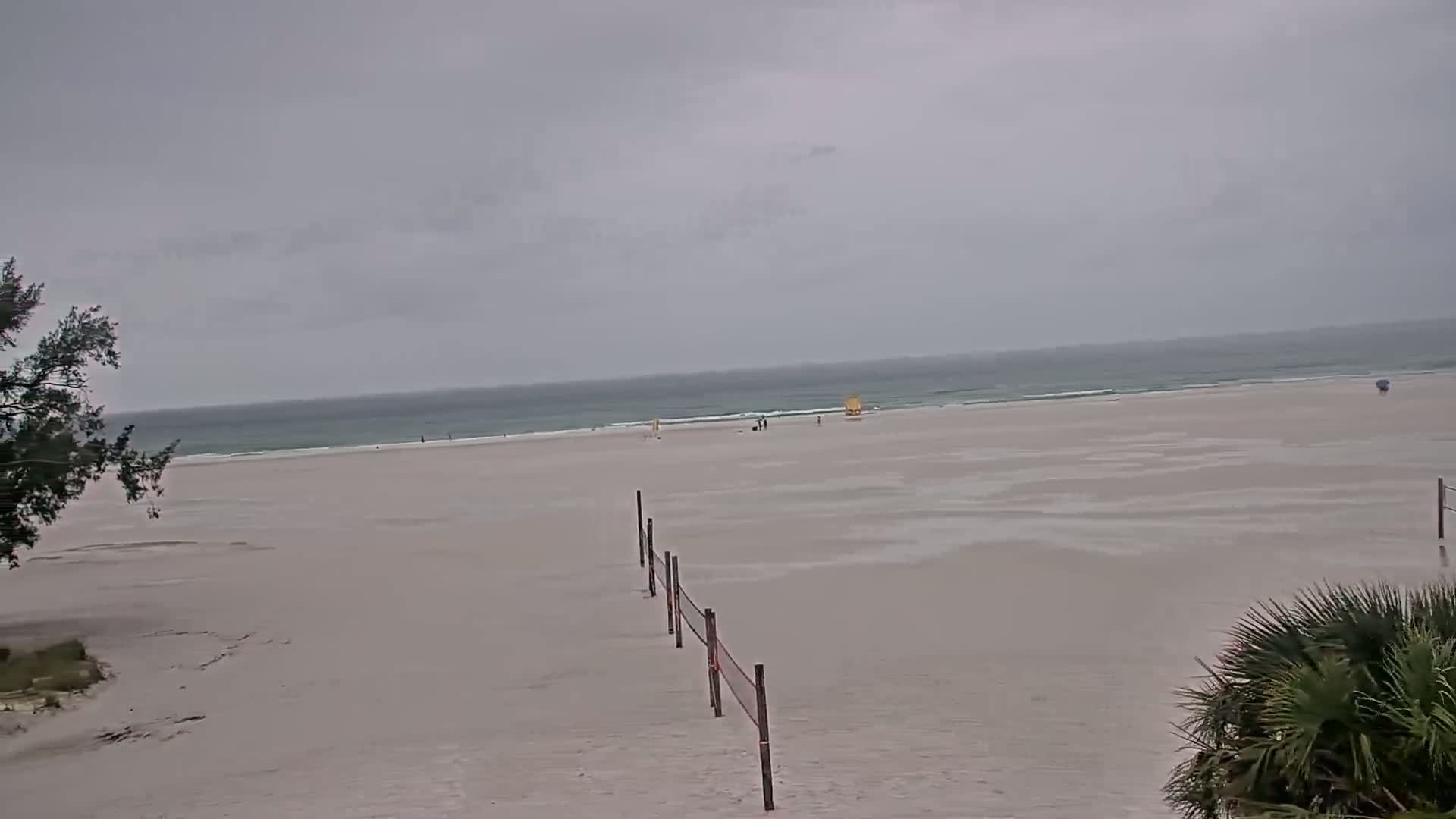 A mostly empty beach with a volleyball net extends into the wet sand under an overcast sky.