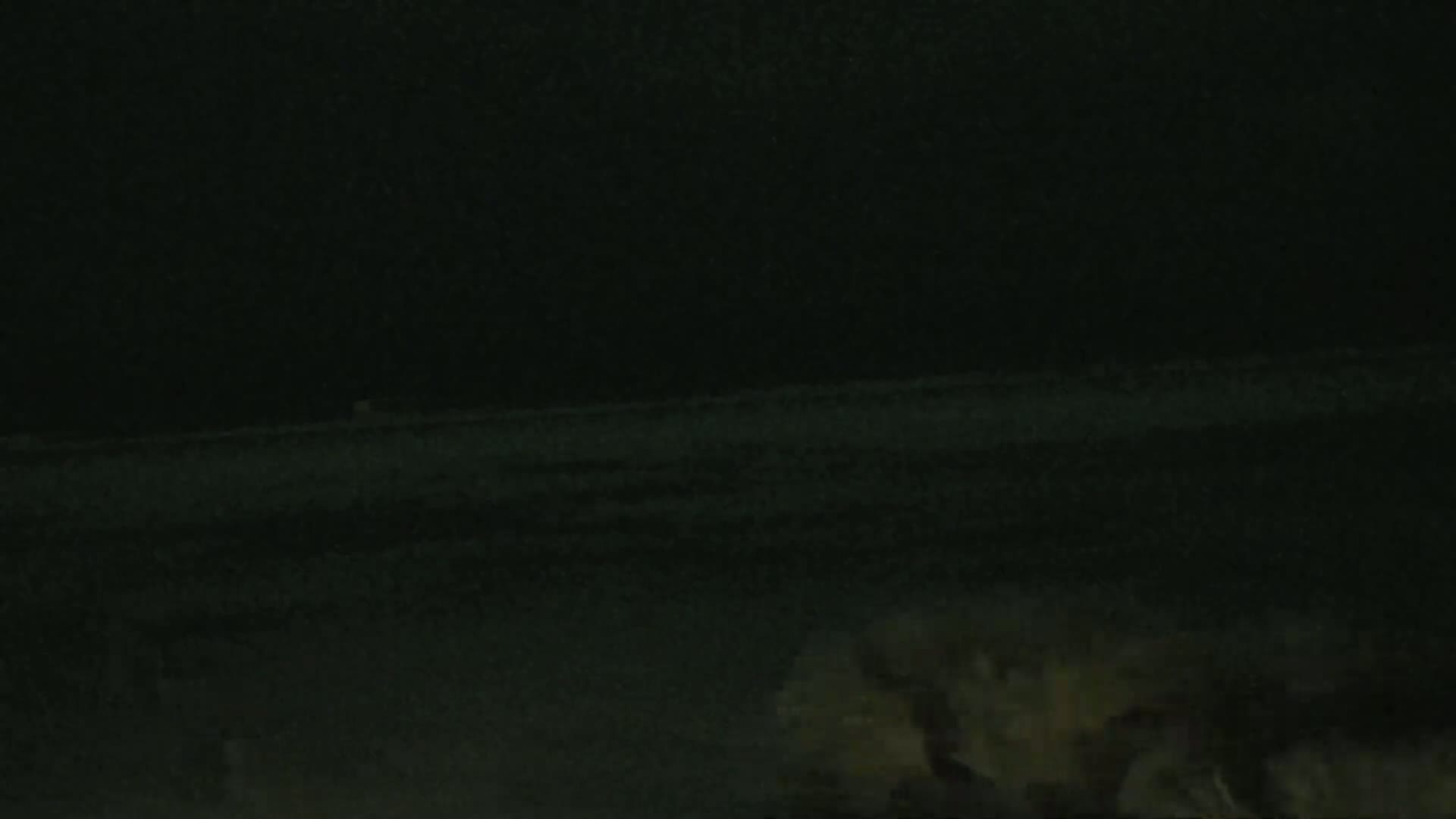 A low-light nighttime image shows a dark, flat expanse of land with indistinct vegetation in the bottom right corner.