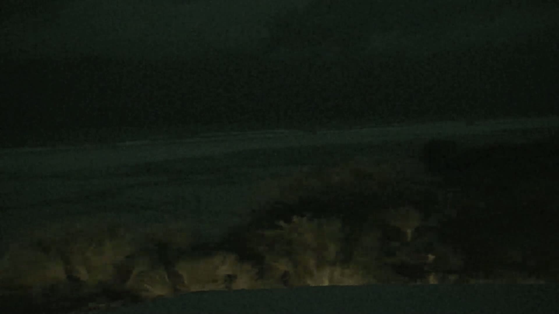 Glowing, light-colored water surges at the base of a dark, nighttime shoreline.