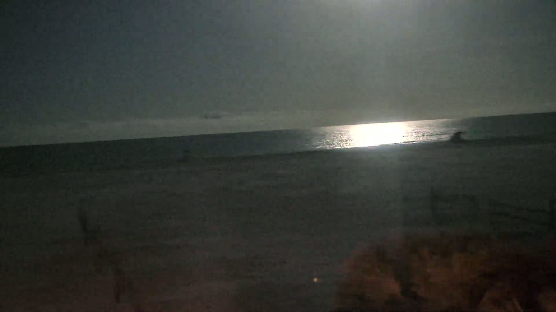 A moonlit beach scene shows a dark ocean reflecting the bright moonlight, with a dark sandy shore in the foreground.