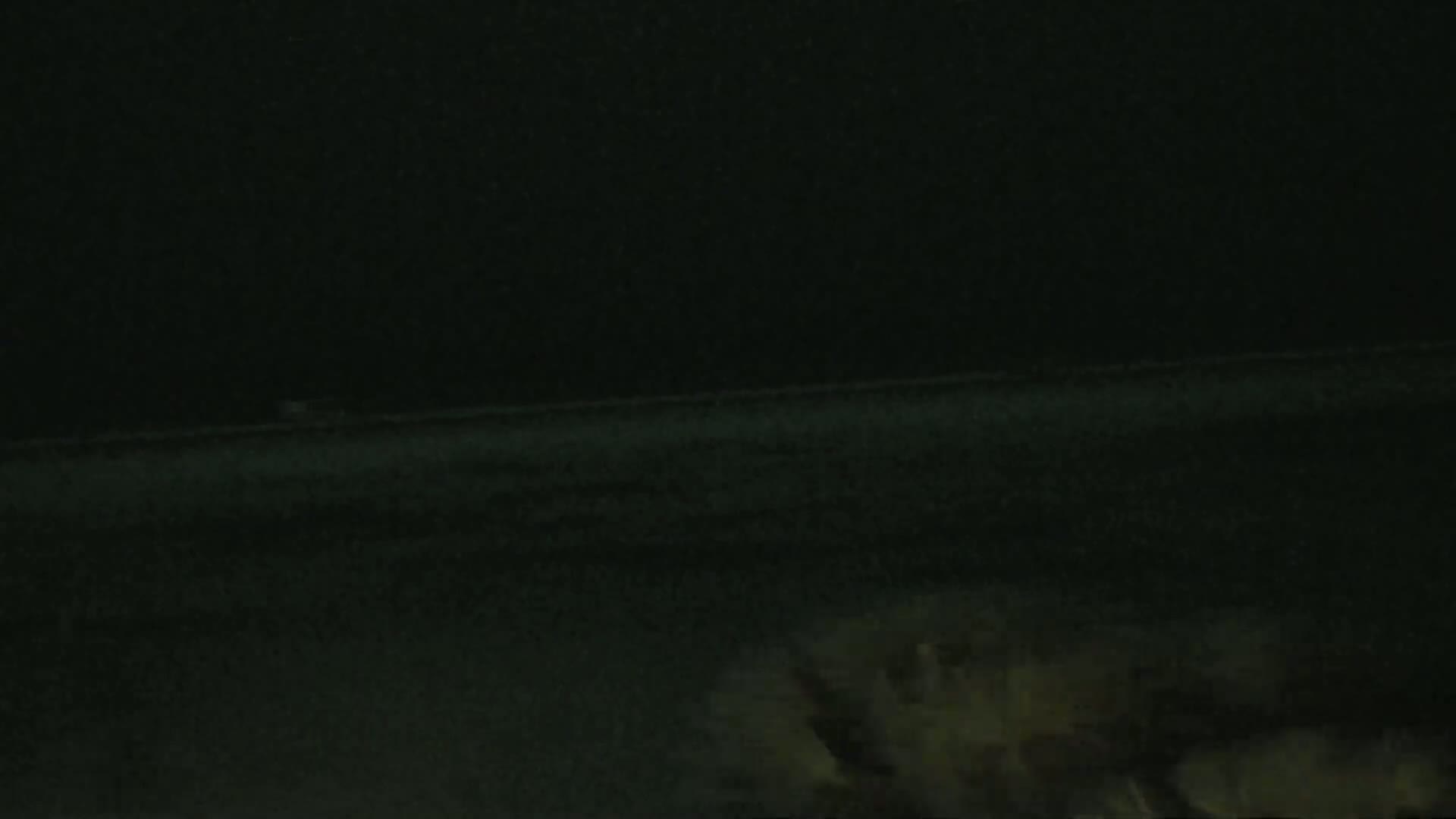 A dark, possibly nighttime scene shows a flat expanse of land or water in the distance, with some indistinct shapes in the foreground.