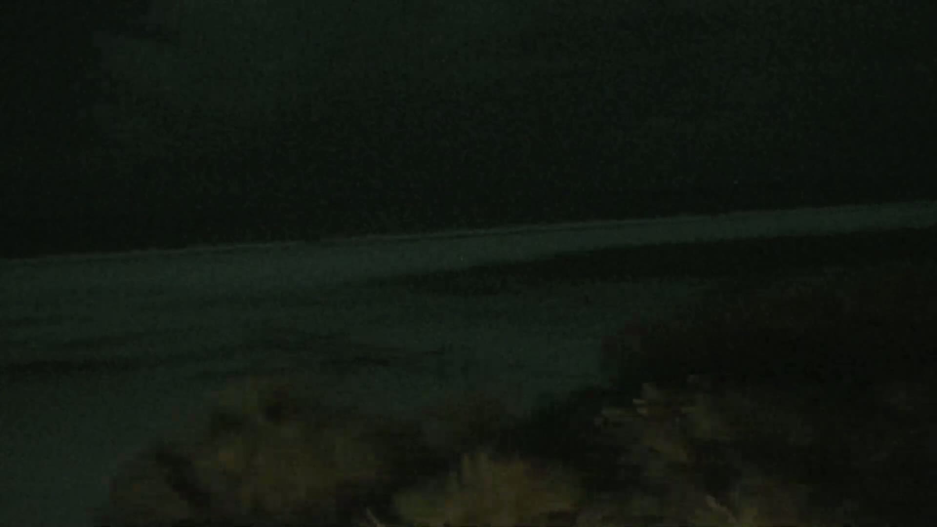 A dark, nighttime scene shows a flat, dark expanse of ground under a completely black sky.