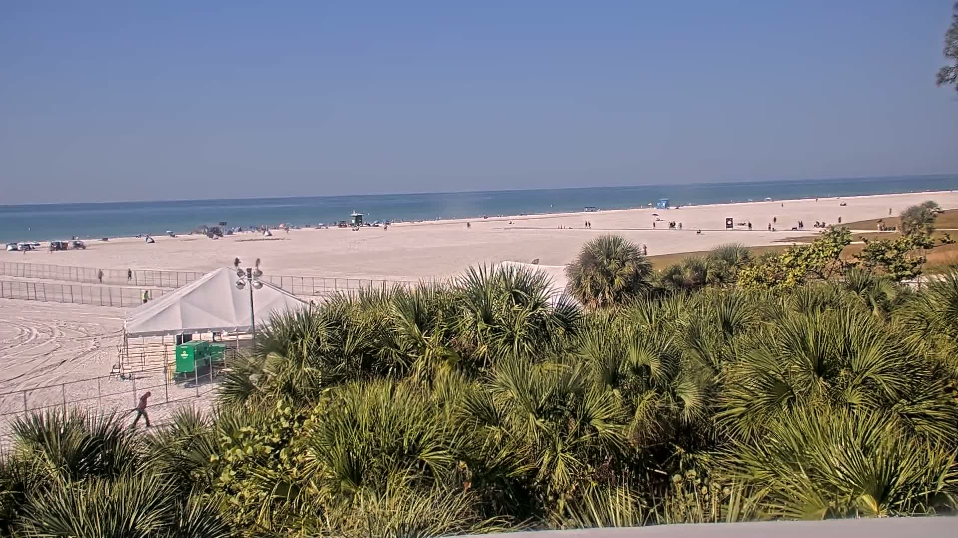 The image displays a sprawling outdoor encampment at night, featuring numerous tents and conical structures on sandy ground, brightly illuminated by a powerful, flaring light source under a clear dark sky.