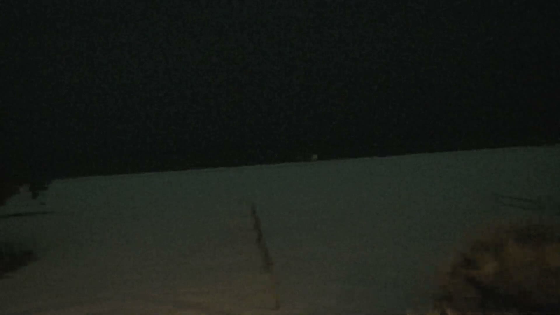 A blurry, dark image depicts a snow-covered landscape under a clear night sky, with a faint distant light on the horizon and indistinct dark shapes in the foreground.