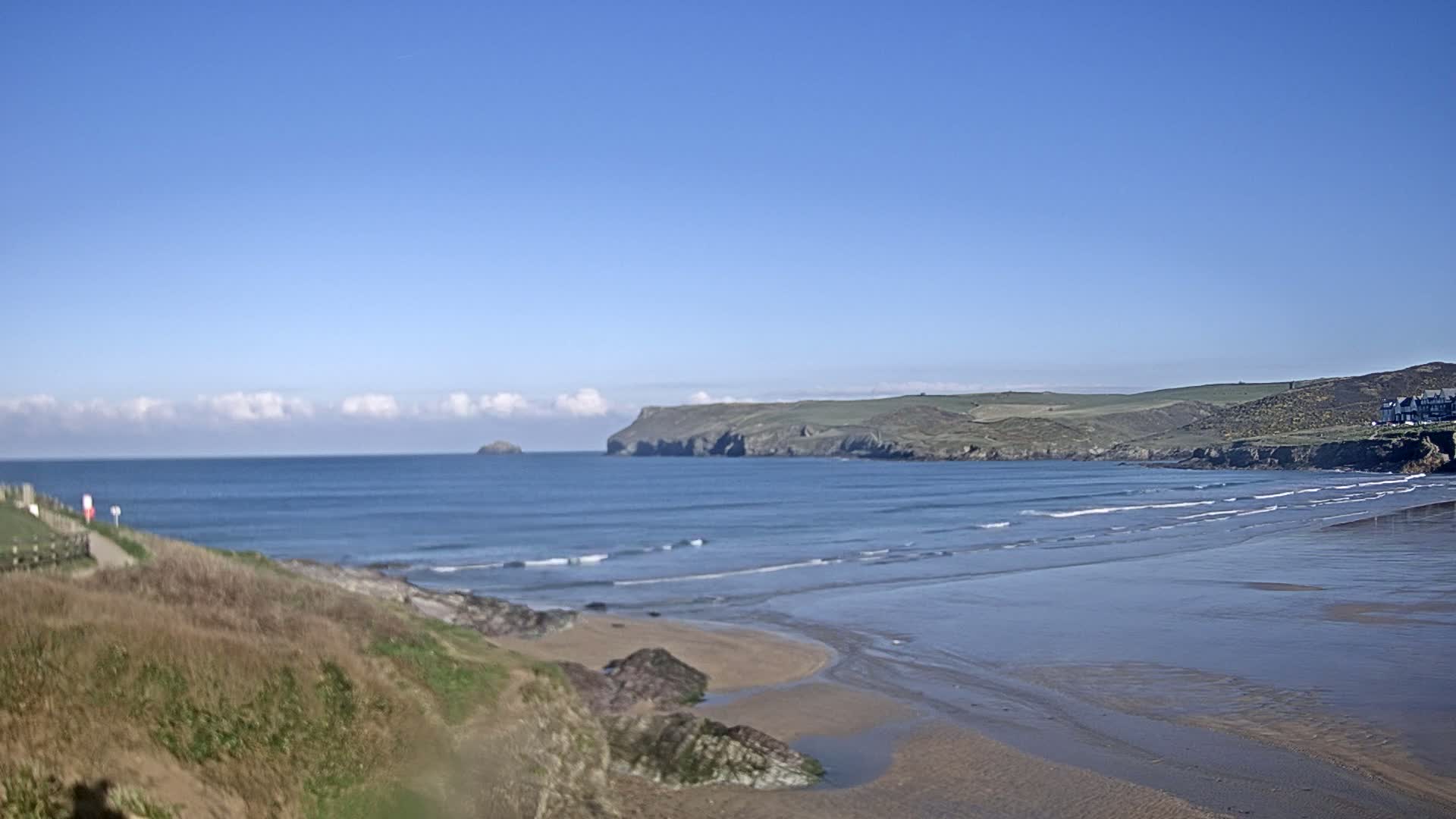 A sandy beach stretches out to a calm ocean under a clear blue sky with a few fluffy clouds.