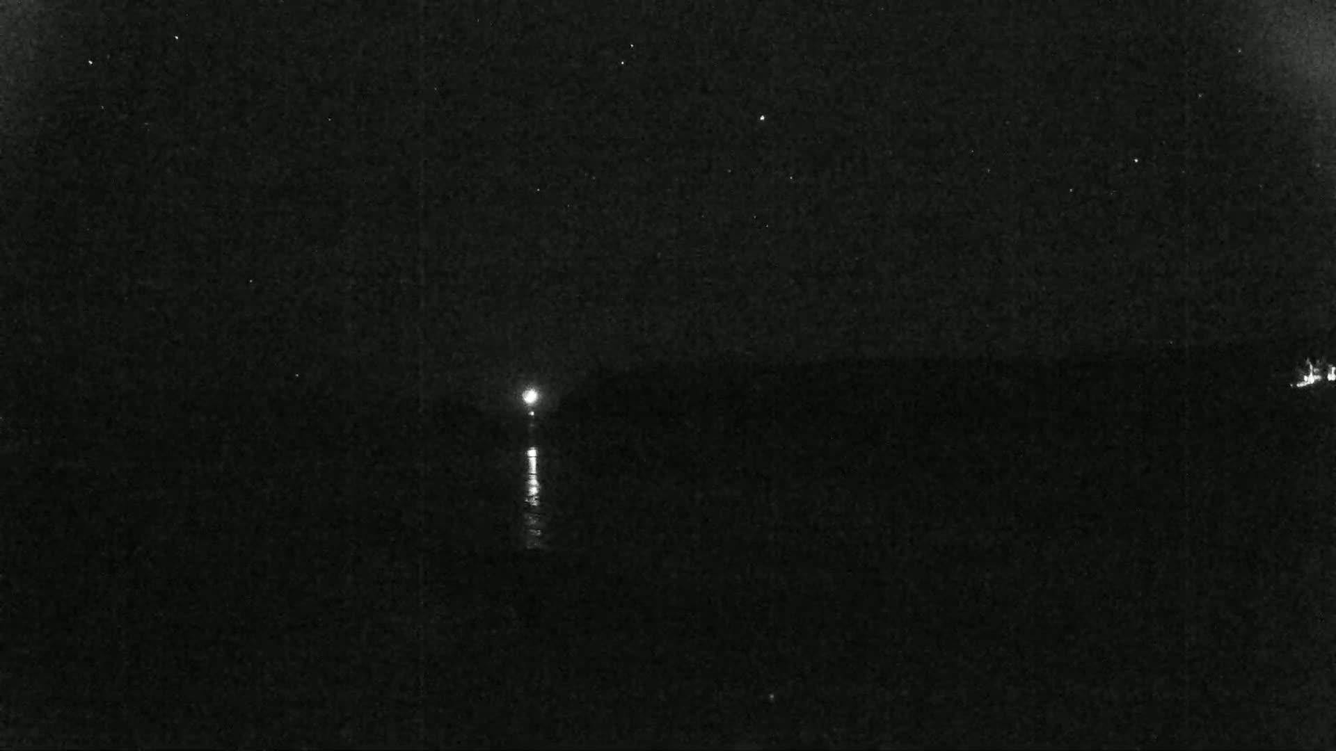 A nighttime view of a body of water with a distant light reflecting on the surface under a clear, starry sky.
