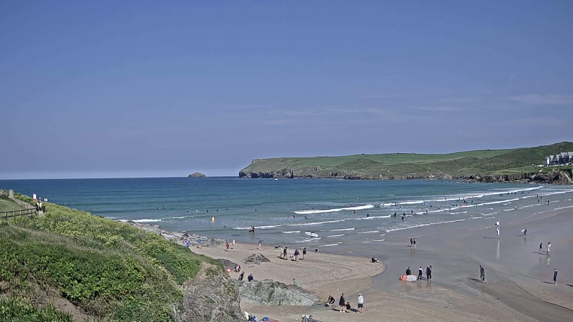 A sandy beach with many surfers in the ocean under a clear blue sky.