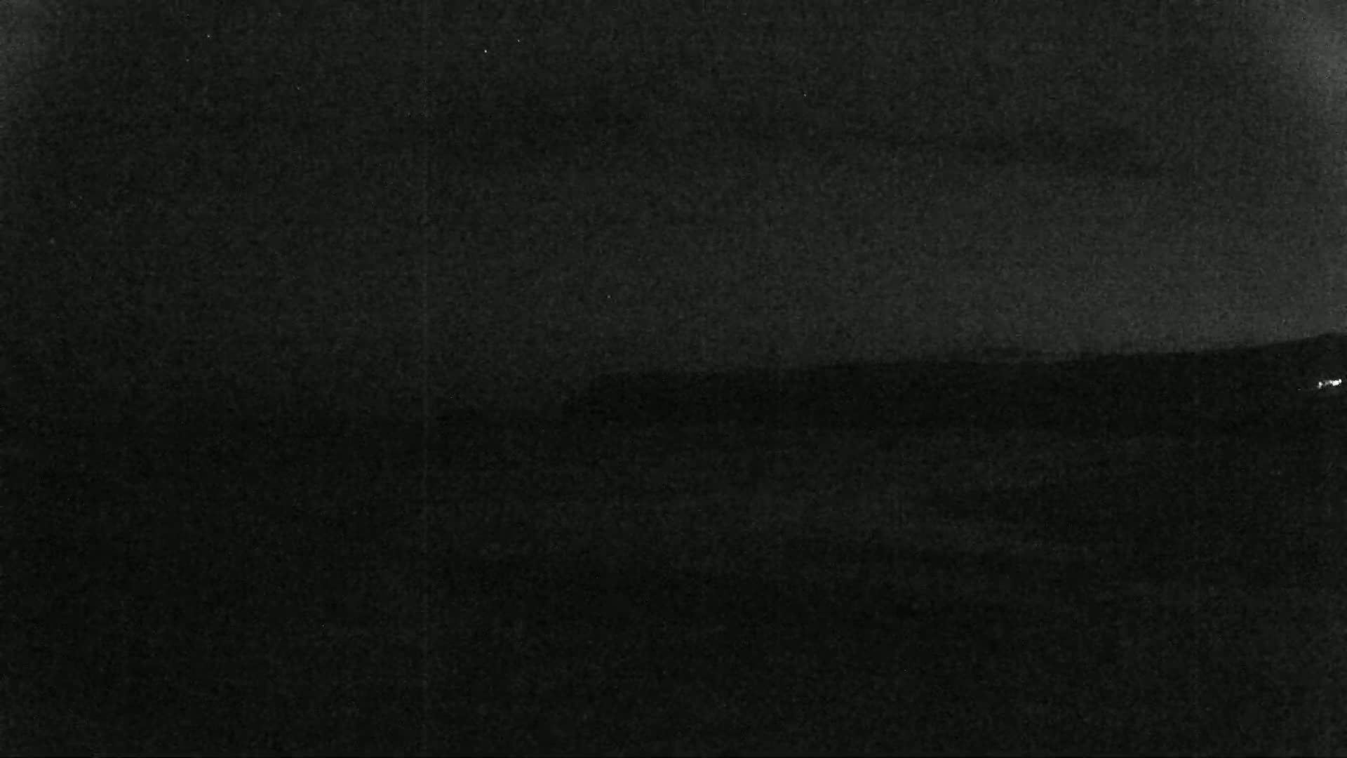 A dark, nighttime landscape shows a low-lying horizon line with a faint, indistinct landmass in the distance under a mostly clear sky.