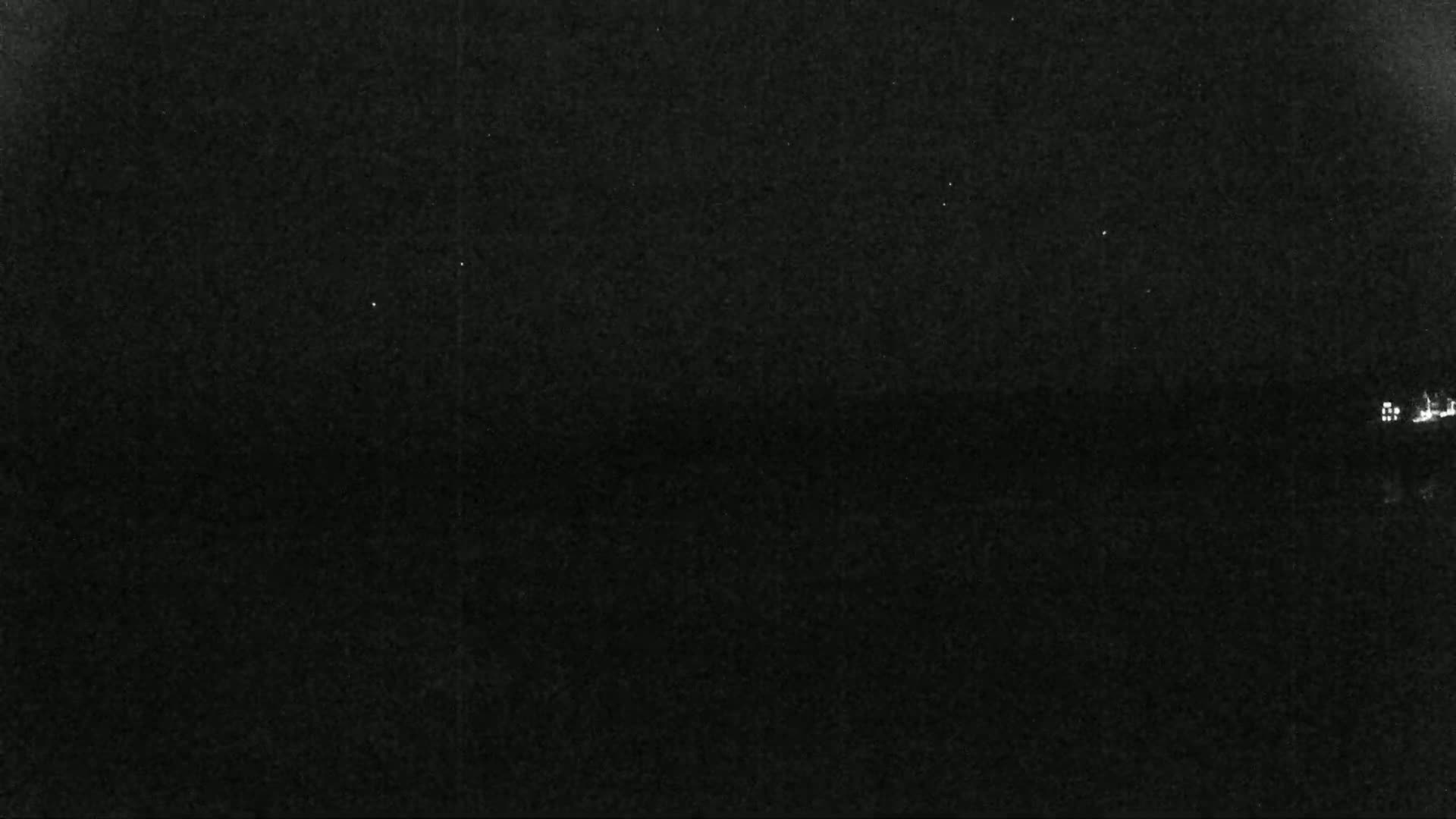 A nighttime, low-light image shows a dark, possibly overcast sky and a few faint lights on the horizon.