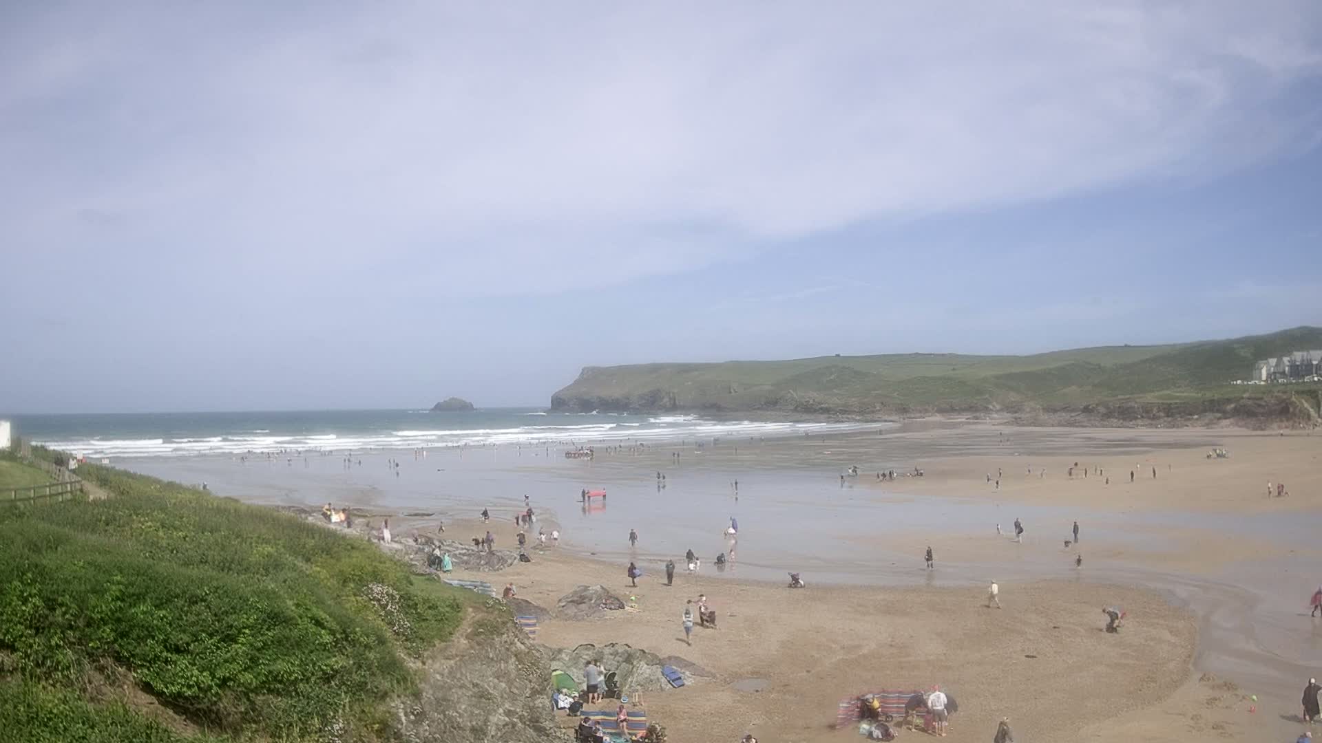 A sandy beach with many people on it and gentle waves under a partly sunny sky.