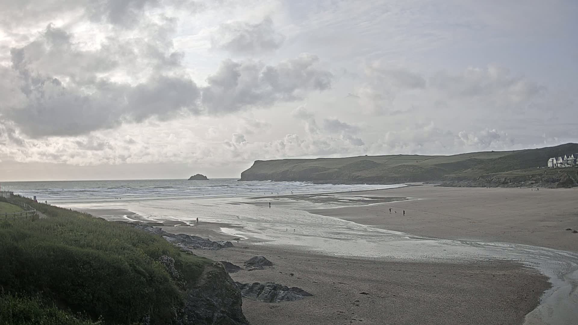 A wide sandy beach stretches out to a calm ocean under a cloudy sky, with a small island visible in the distance.