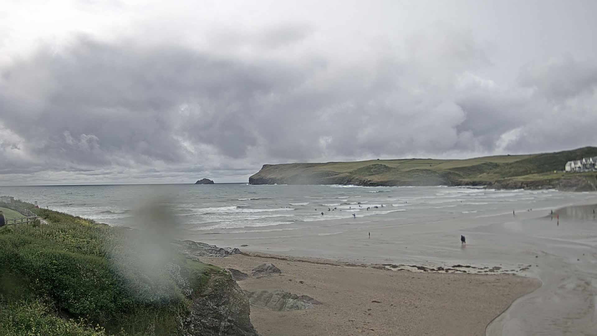 A sandy beach with small waves and several people in the water is visible under a cloudy sky.