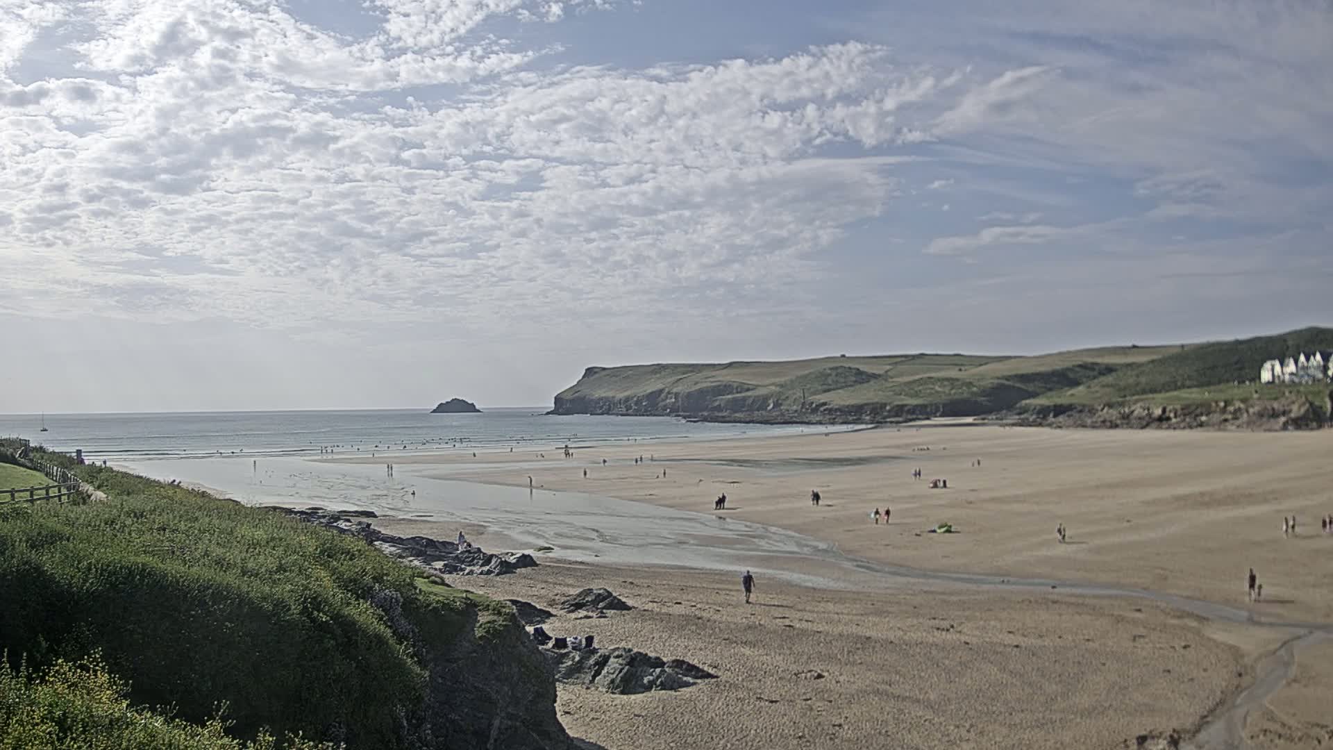 A sandy beach with scattered people stretches to a calm ocean under a partly cloudy sky.