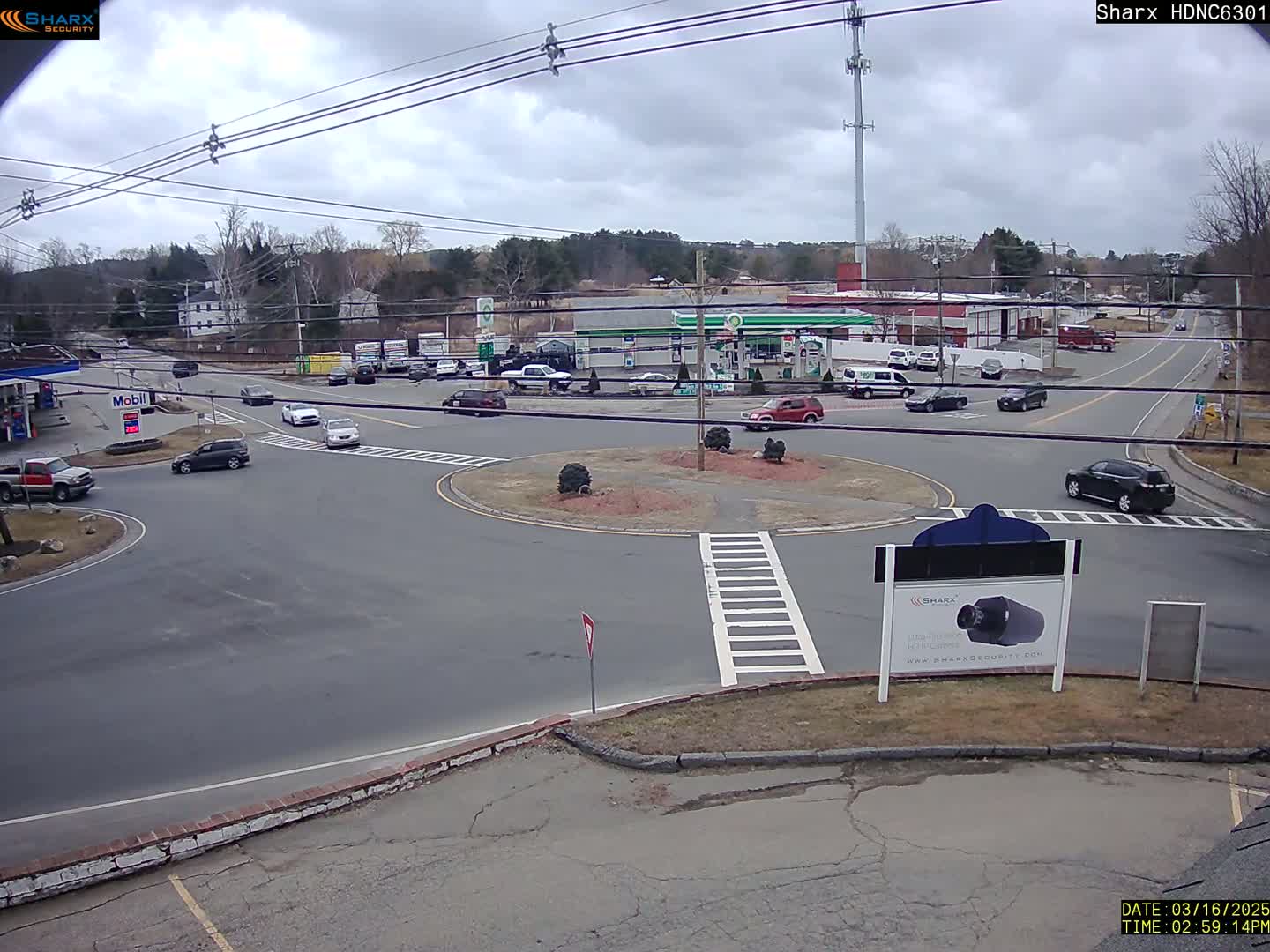 A roundabout with several cars and a gas station is visible under an overcast sky.