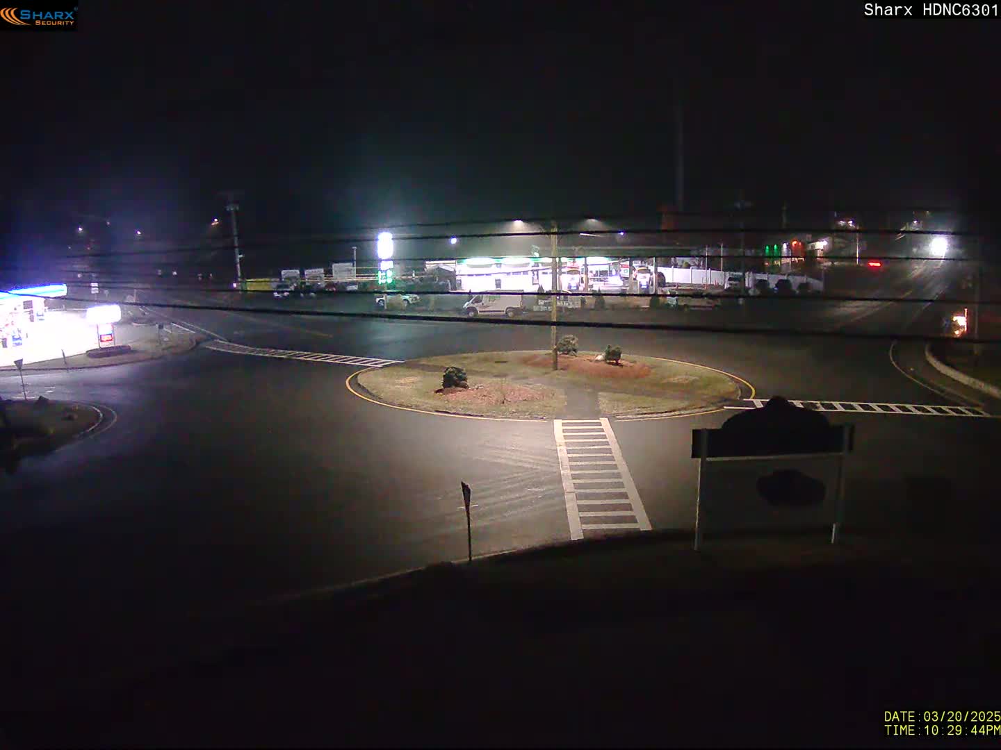 A nighttime view of a gas station and roundabout with minimal traffic under foggy conditions.