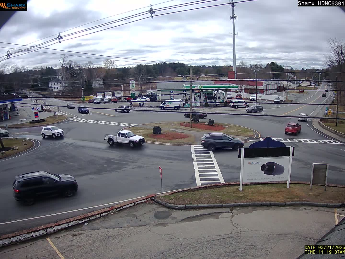 Several vehicles are navigating a roundabout and nearby roads on an overcast day.