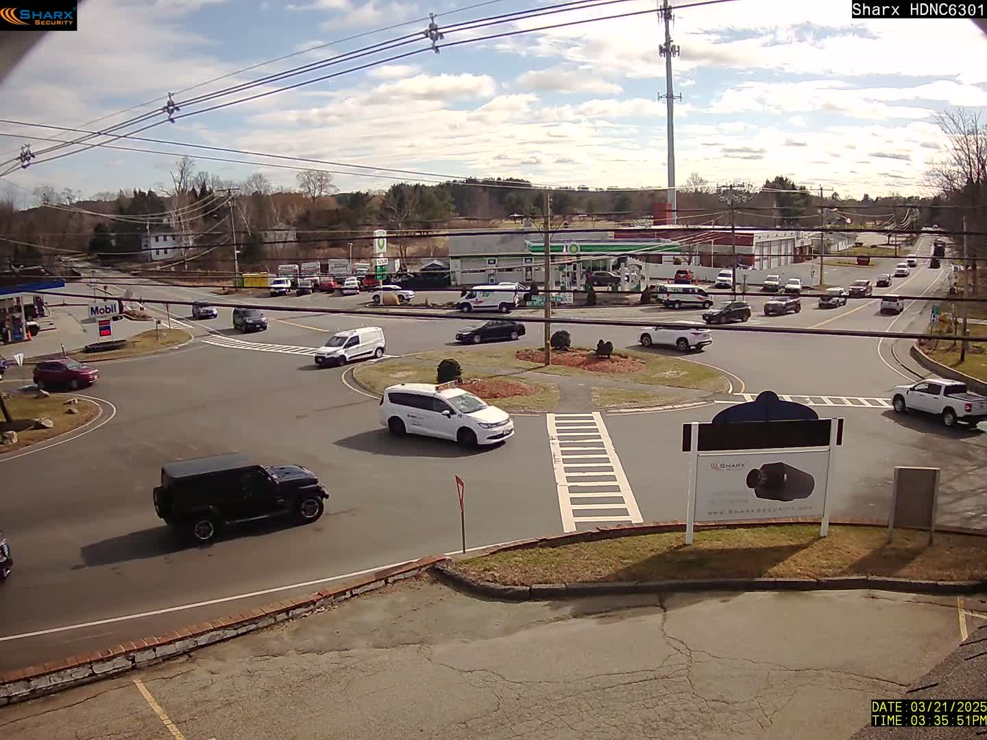 A sunny day reveals a traffic circle with several vehicles, surrounded by businesses and residential areas.