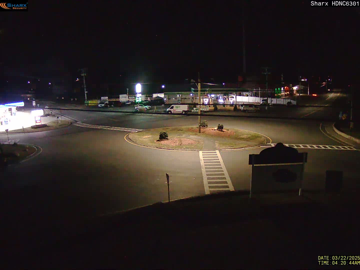 A nighttime view of a roundabout intersection near a gas station and other businesses under clear skies.