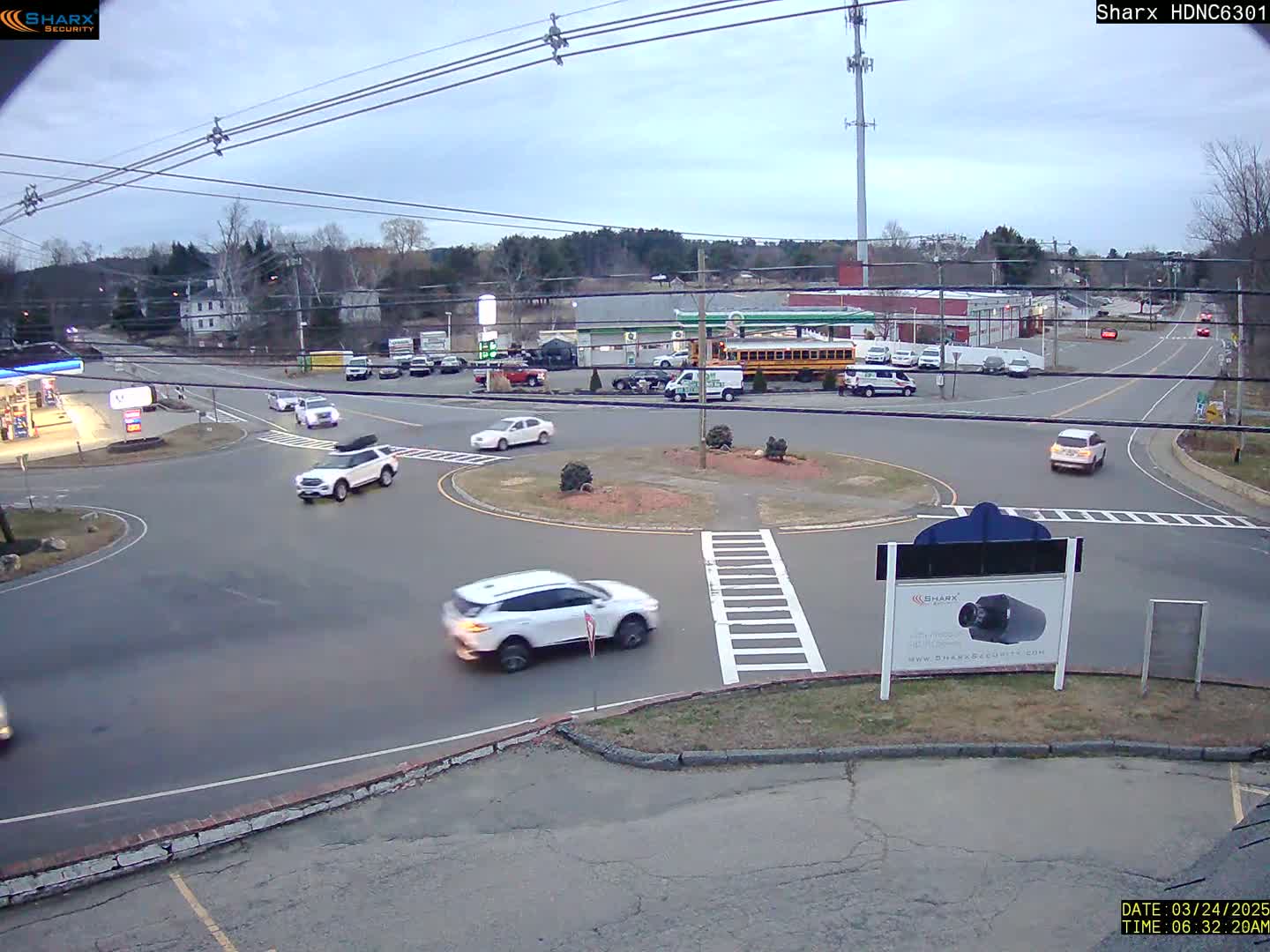Several cars are navigating a roundabout at dusk under a cloudy sky.