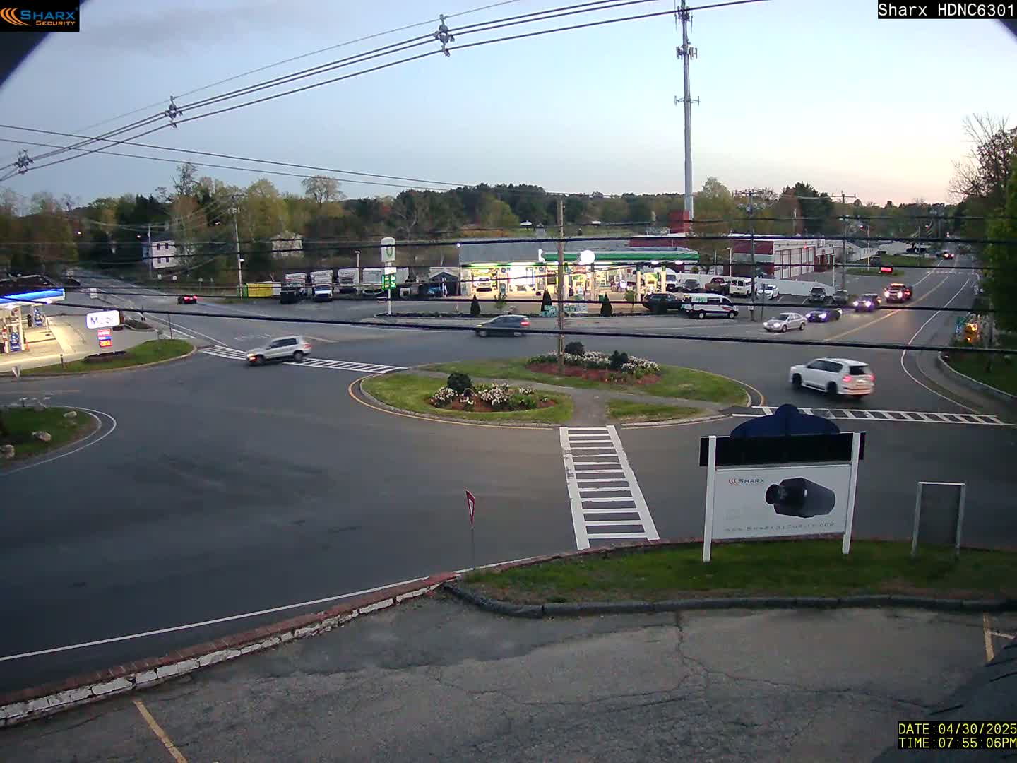 A twilight scene shows a roundabout with several cars and a gas station, surrounded by trees and buildings.