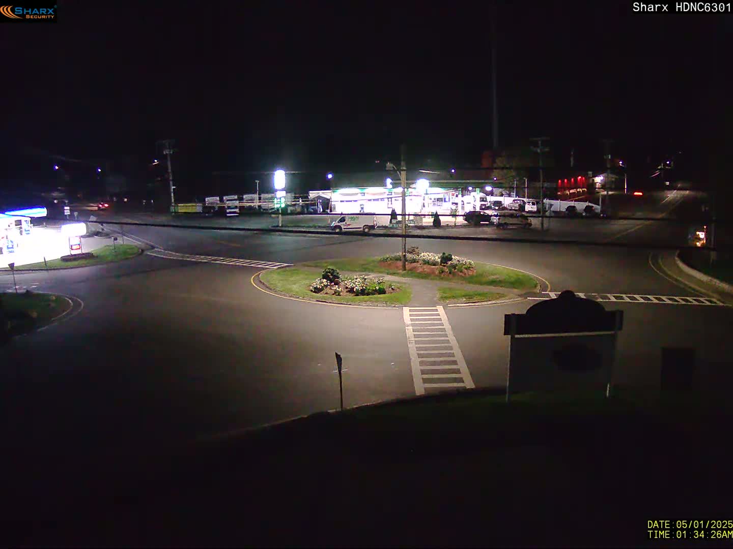 A nighttime view of a gas station and traffic circle with minimal vehicle activity under dark skies.
